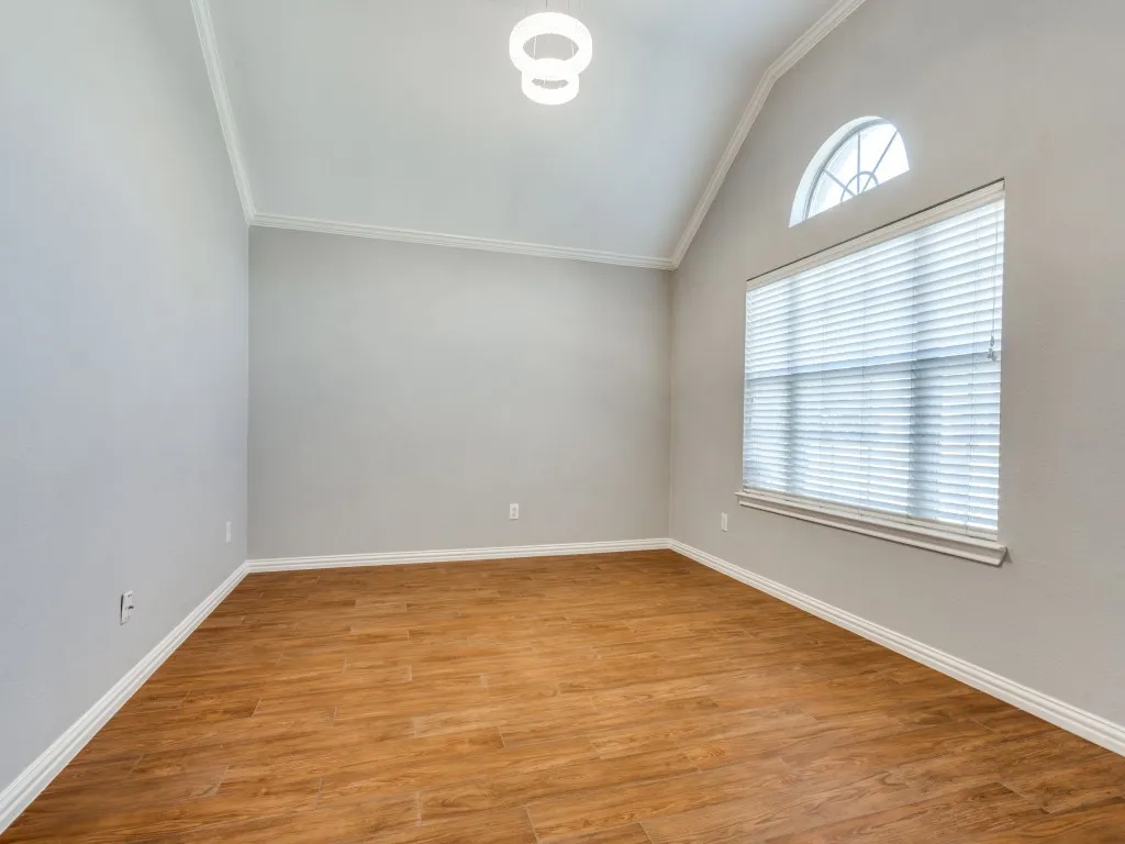 Unfurnished room featuring light wood finished floors, baseboards, crown molding, and lofted ceiling