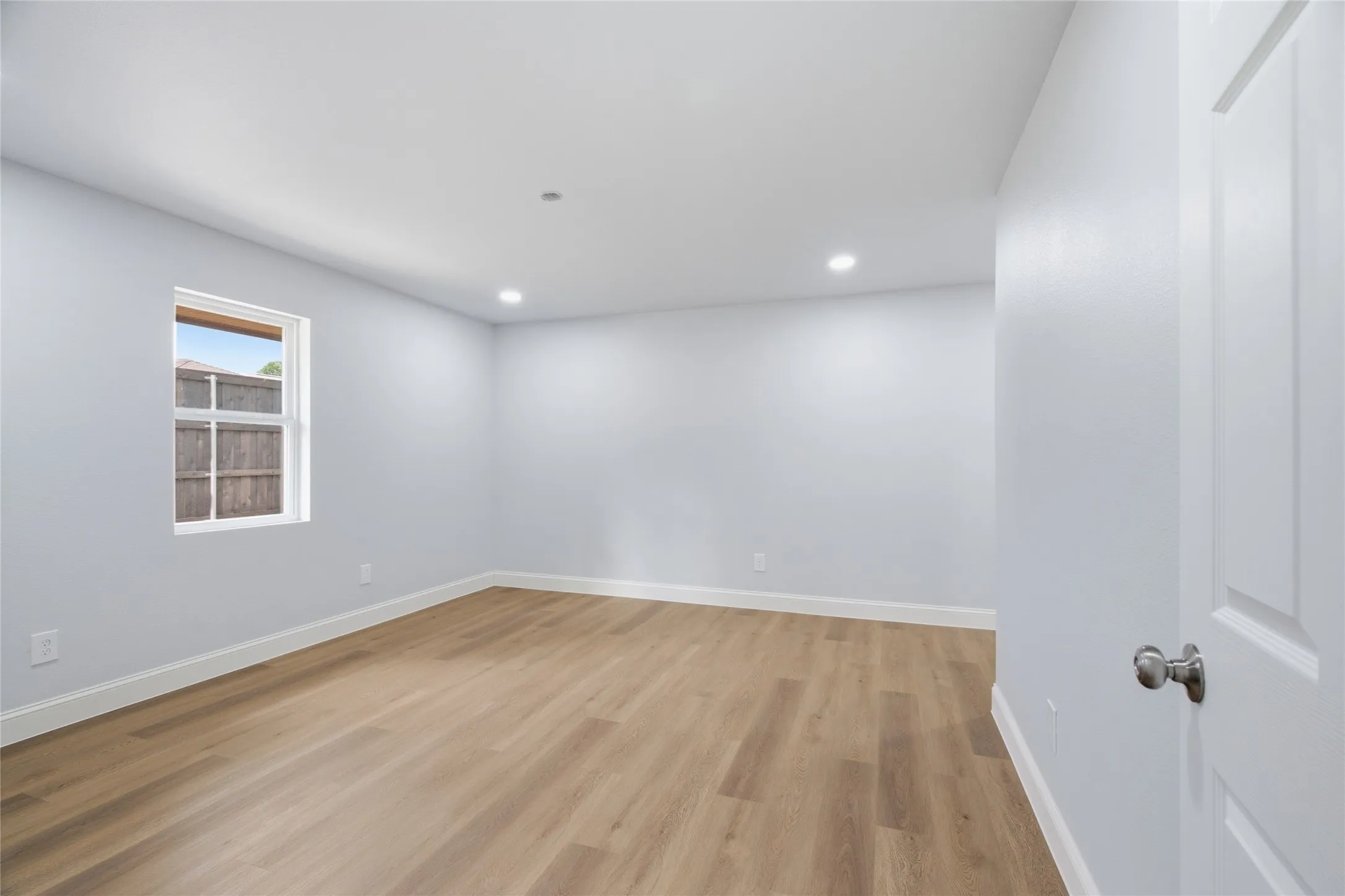 Room featuring wood-finish flooring, recessed lighting, and a window with white trim