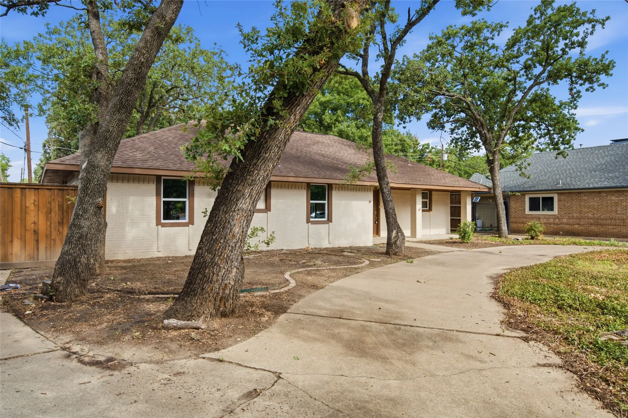 Single-story residence featuring a neutral-toned exterior, a brown shingle roof, and multiple mature trees
