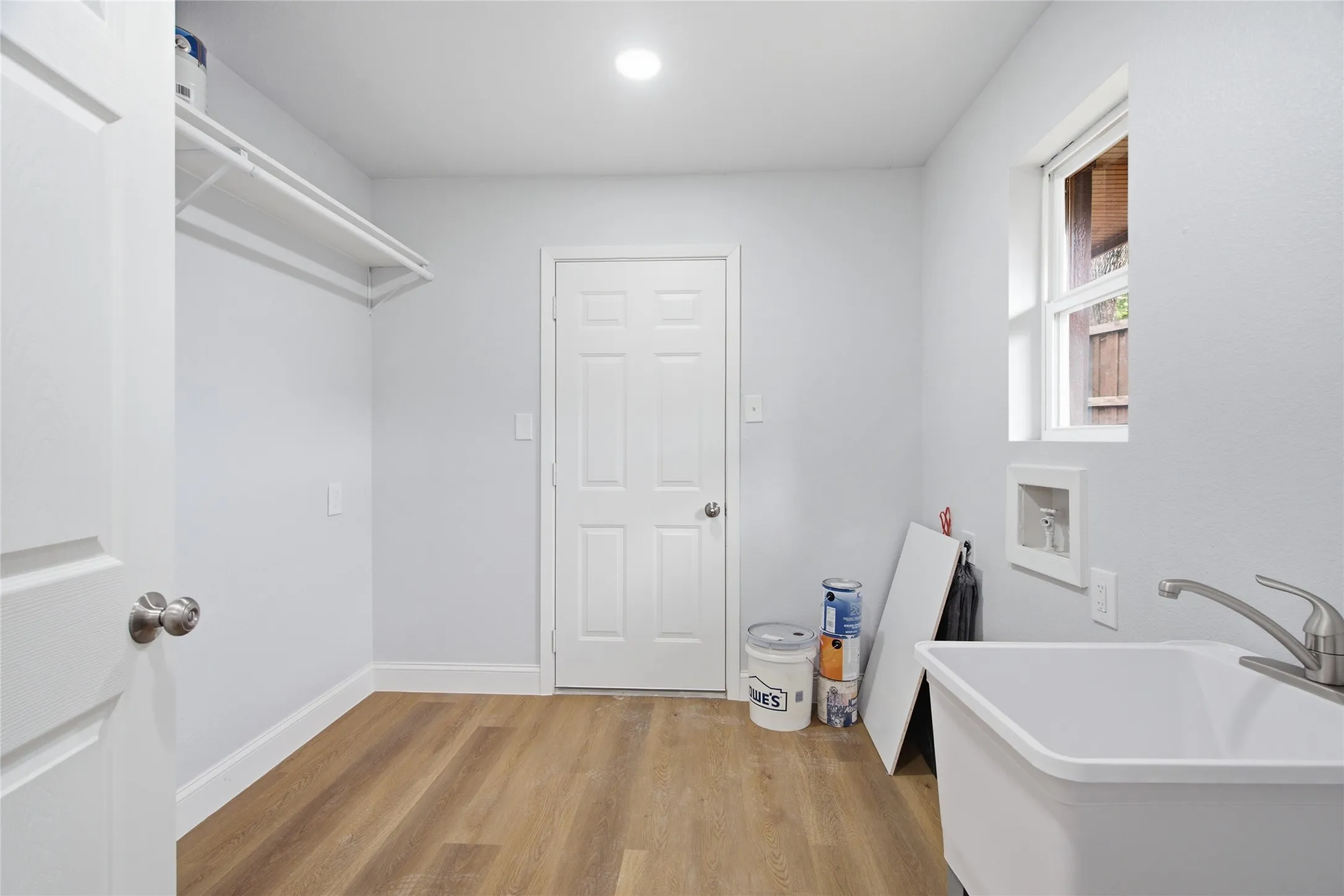 Dedicated utility space featuring wood-finish flooring, a utility sink with a brushed nickel faucet, and a wall-mounted shelf