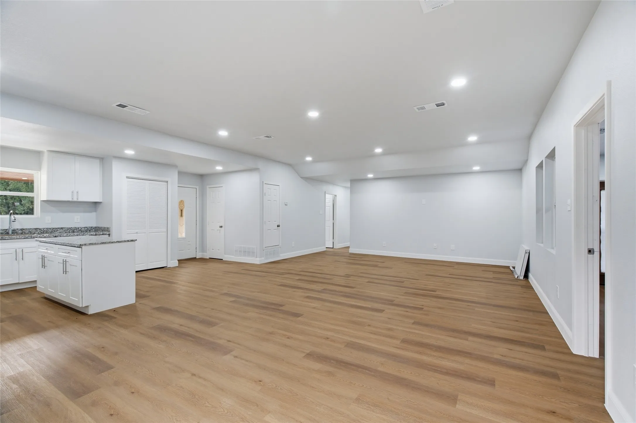 Open-concept living space featuring wood-finish flooring, recessed lighting, and a kitchen island with a granite countertop