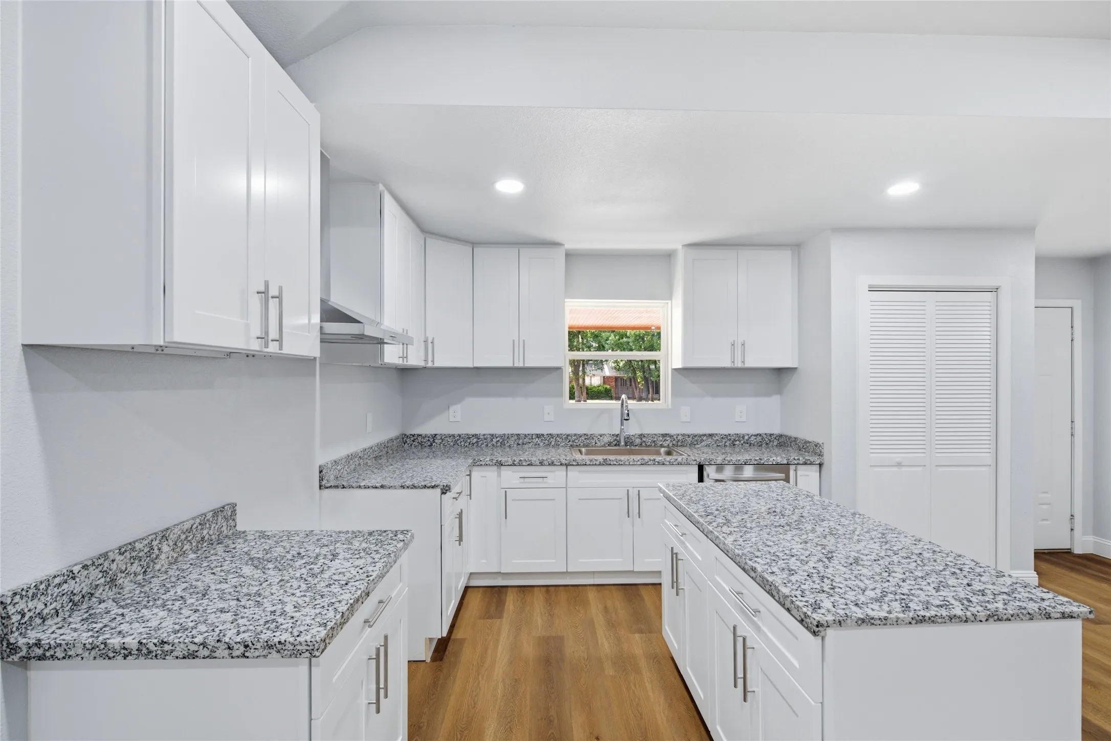 Modern kitchen featuring white cabinetry, granite-style countertops, wood-finish flooring, a central island, and built-in overhead lighting