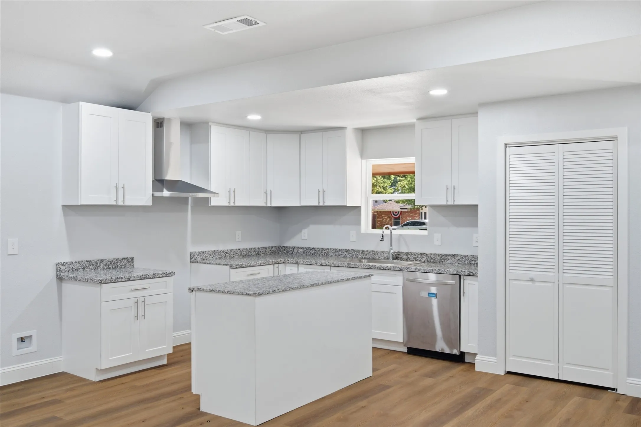 Modern kitchen featuring white cabinetry, light-toned granite-style countertops, stainless steel appliances, a center island, and wood-finish flooring
