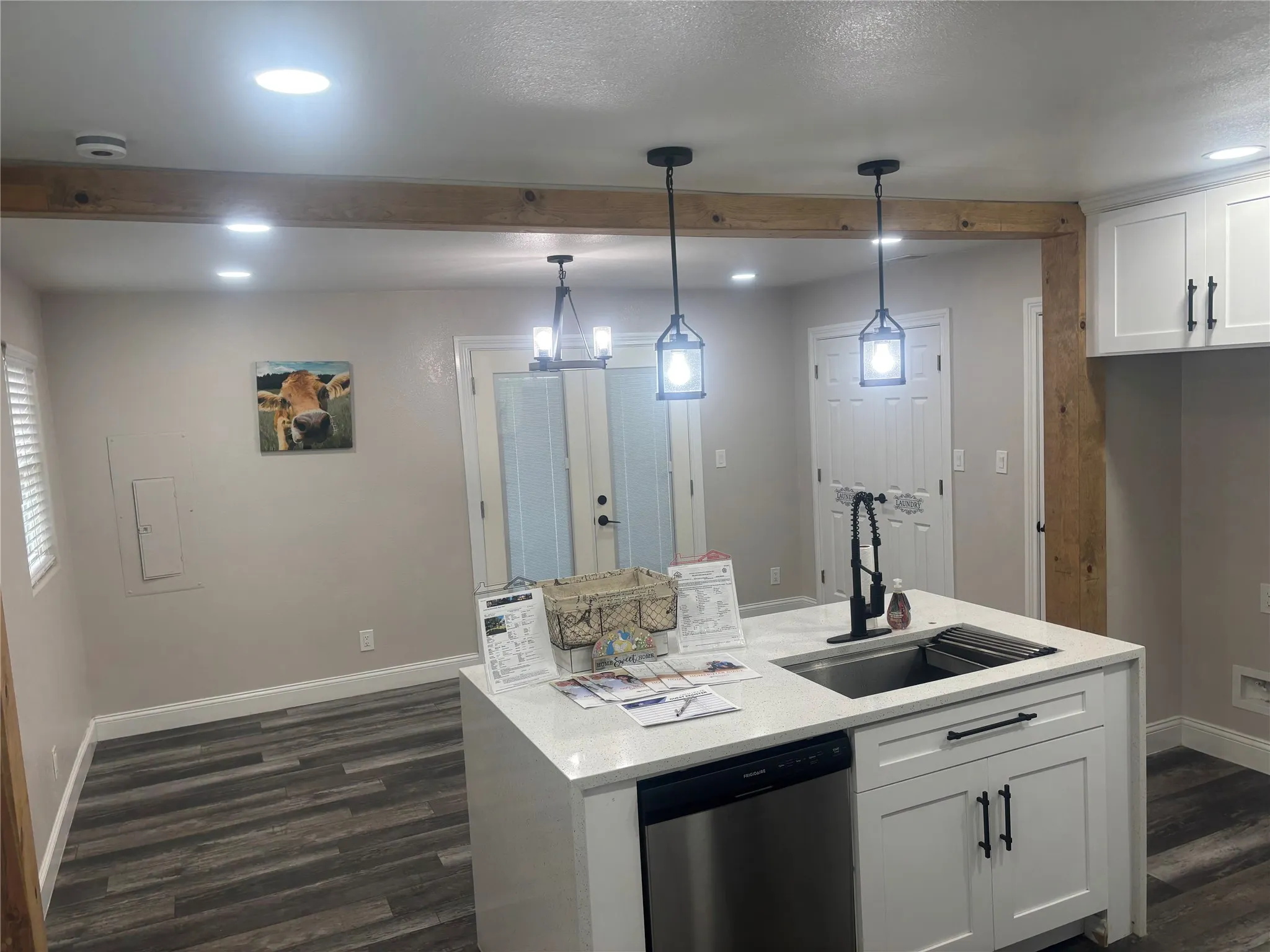 Kitchen island featuring a stainless steel sink, white shaker cabinetry with black hardware, and an integrated dishwasher