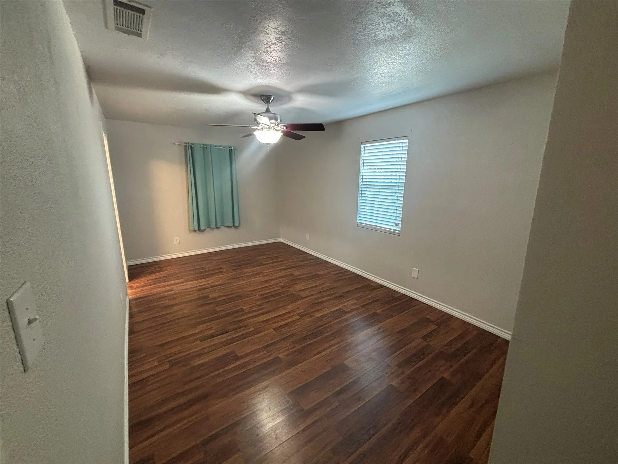 Spacious room featuring wood-finish flooring, light-colored walls, and a ceiling fan with integrated lighting