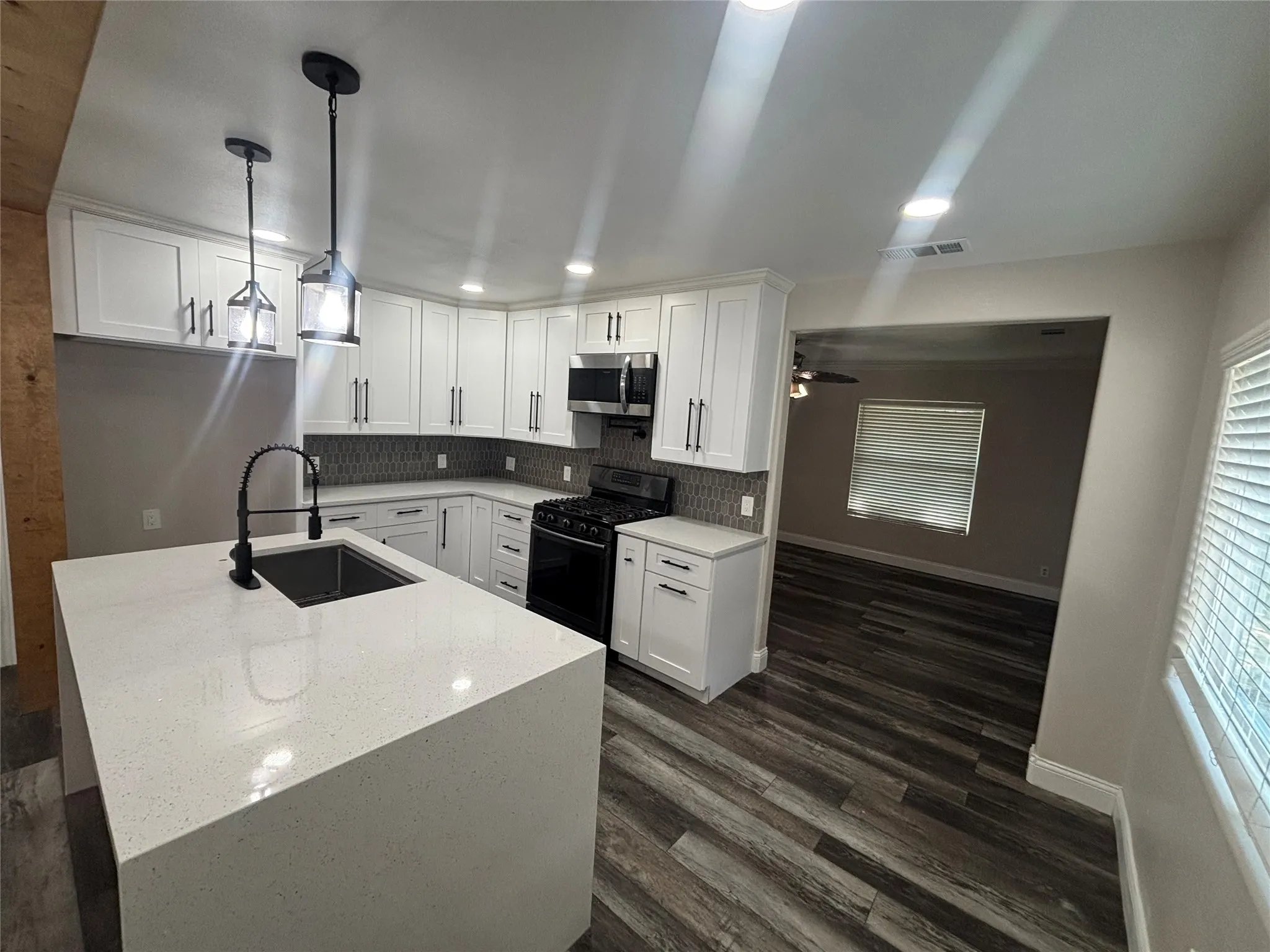 Modern kitchen featuring white shaker cabinetry, an integrated island with a waterfall countertop, and a black gooseneck faucet
