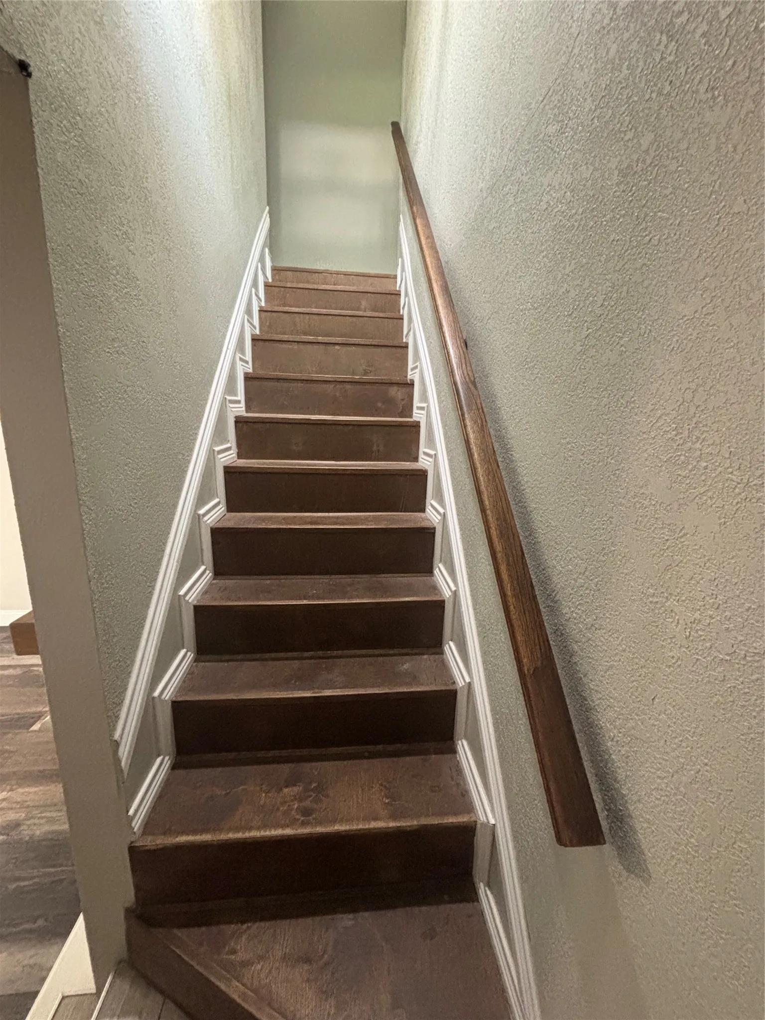 Staircase featuring wood-finish treads, white risers, and a dark wood-finish handrail