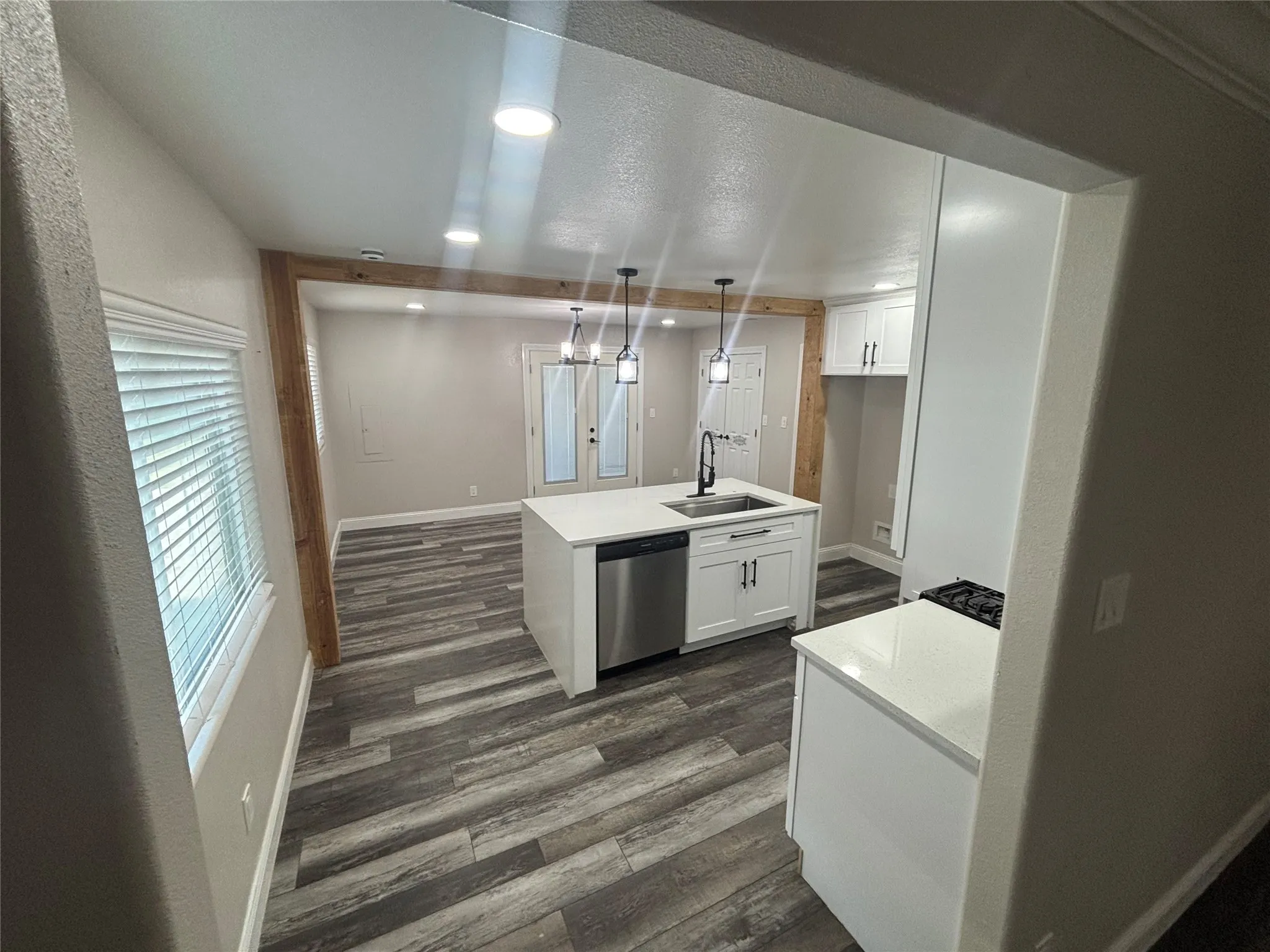 Open-concept kitchen featuring a central island with an undermount sink, stainless steel dishwasher, and white shaker cabinetry