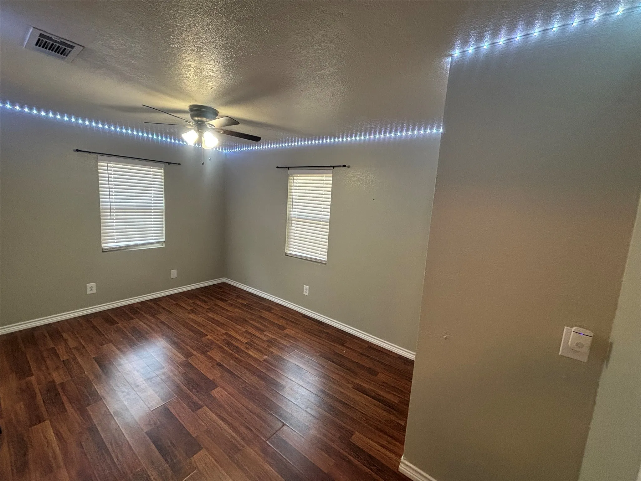 Spacious room featuring wood-finish flooring, two windows with blinds, a ceiling fan, and crown molding