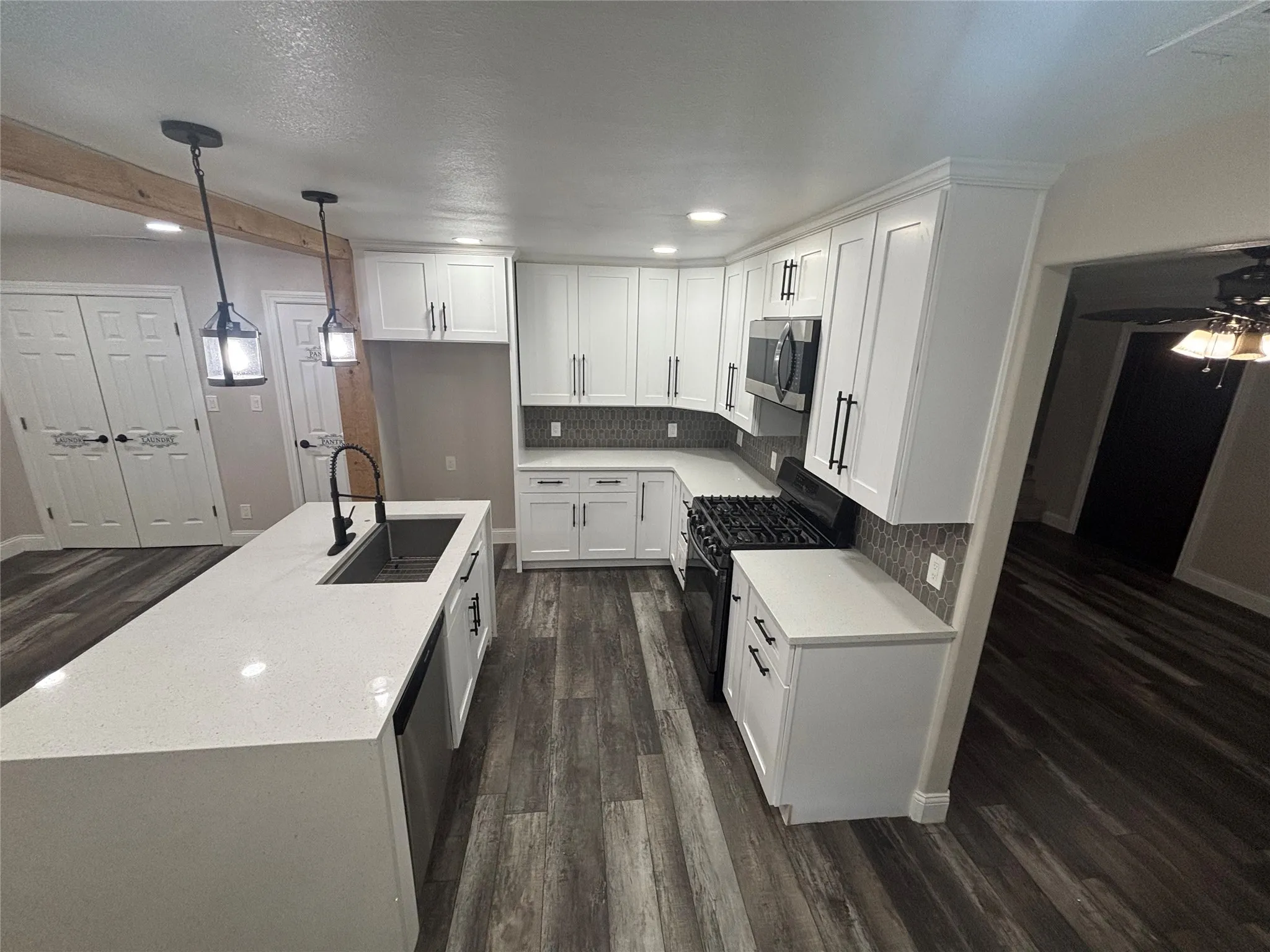 Modern kitchen featuring white cabinetry with matte black hardware, quartz countertops, stainless steel appliances including a built-in microwave and gas range, and wood-finish flooring