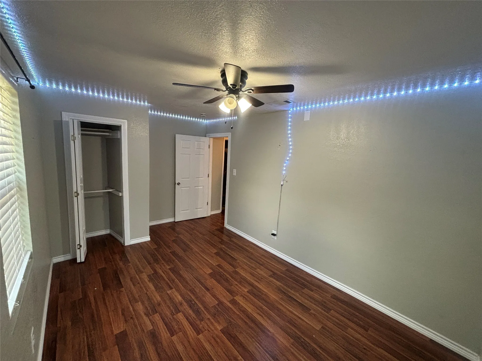 Room featuring wood-finish flooring, a ceiling fan with integrated lighting, a built-in closet with double doors, and a window with horizontal blinds
