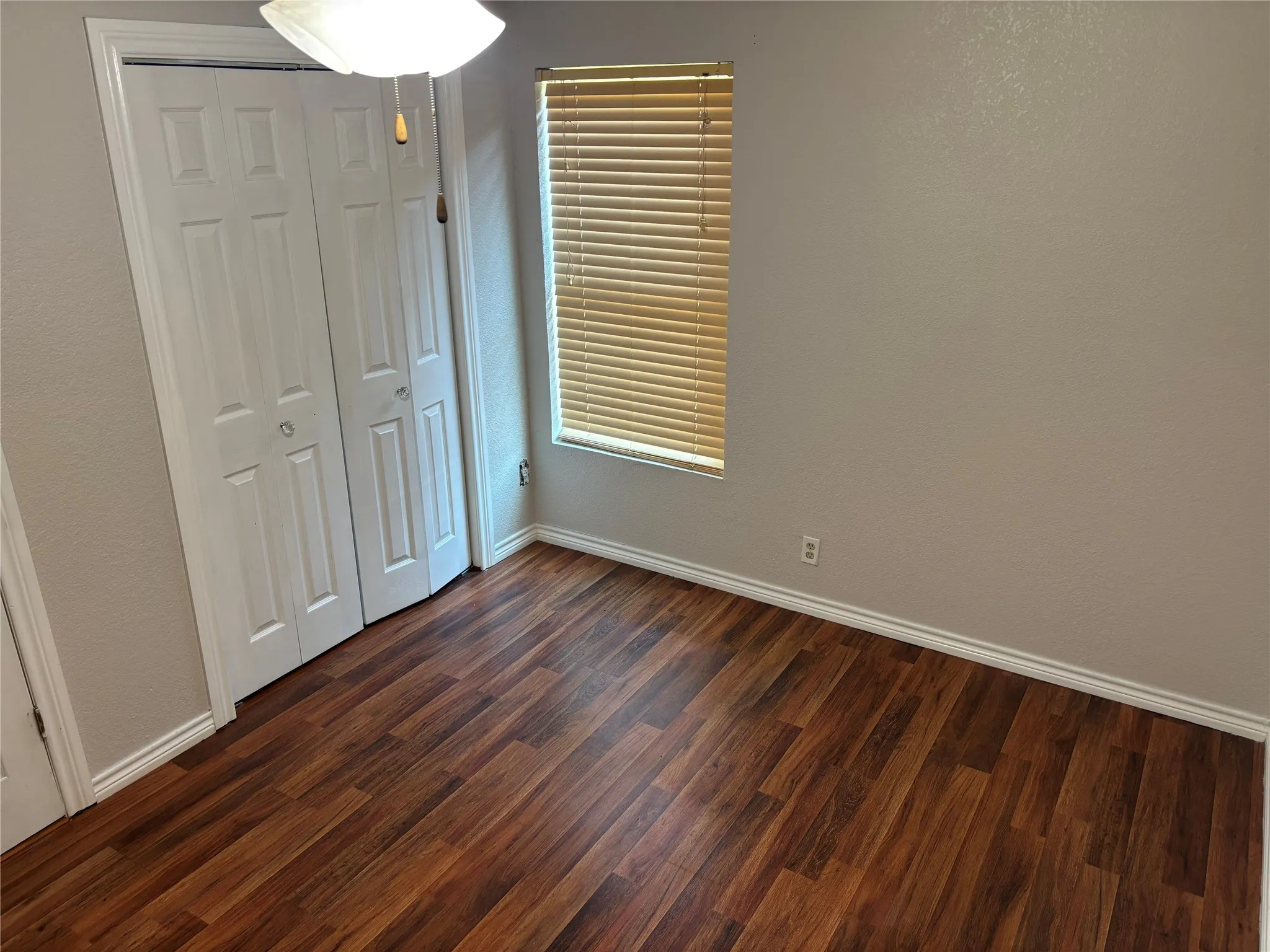 Interior room featuring wood-finish flooring, light neutral-toned walls, and a window with horizontal blinds