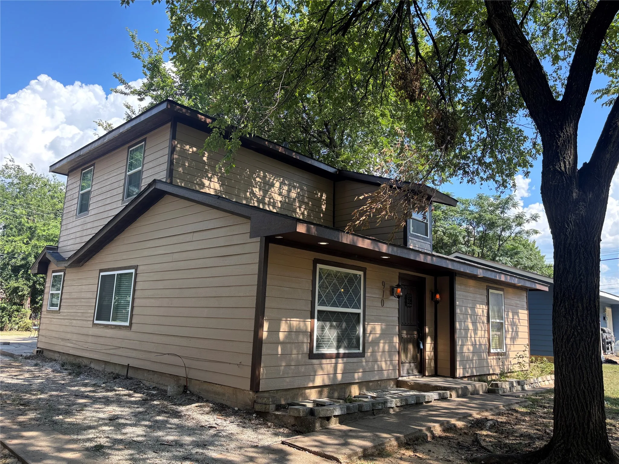 Two-story residence featuring tan horizontal siding with dark trim, multiple rooflines, a covered entry with dual outdoor wall lanterns, and a front door with a unique vertical wood panel design