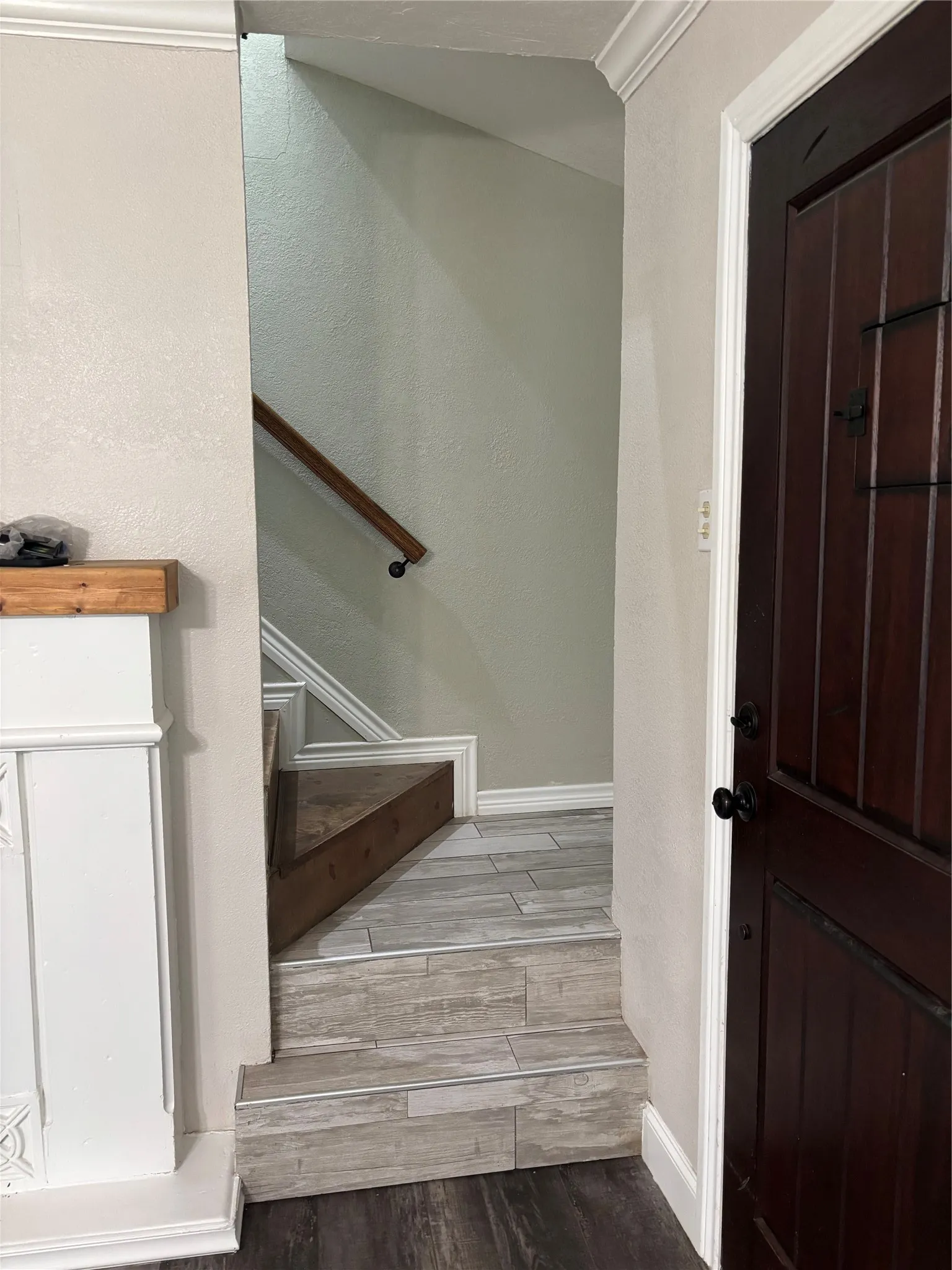 Entryway featuring a dark wood-finish door, white trim, and a staircase with wood-finish flooring and a wood handrail