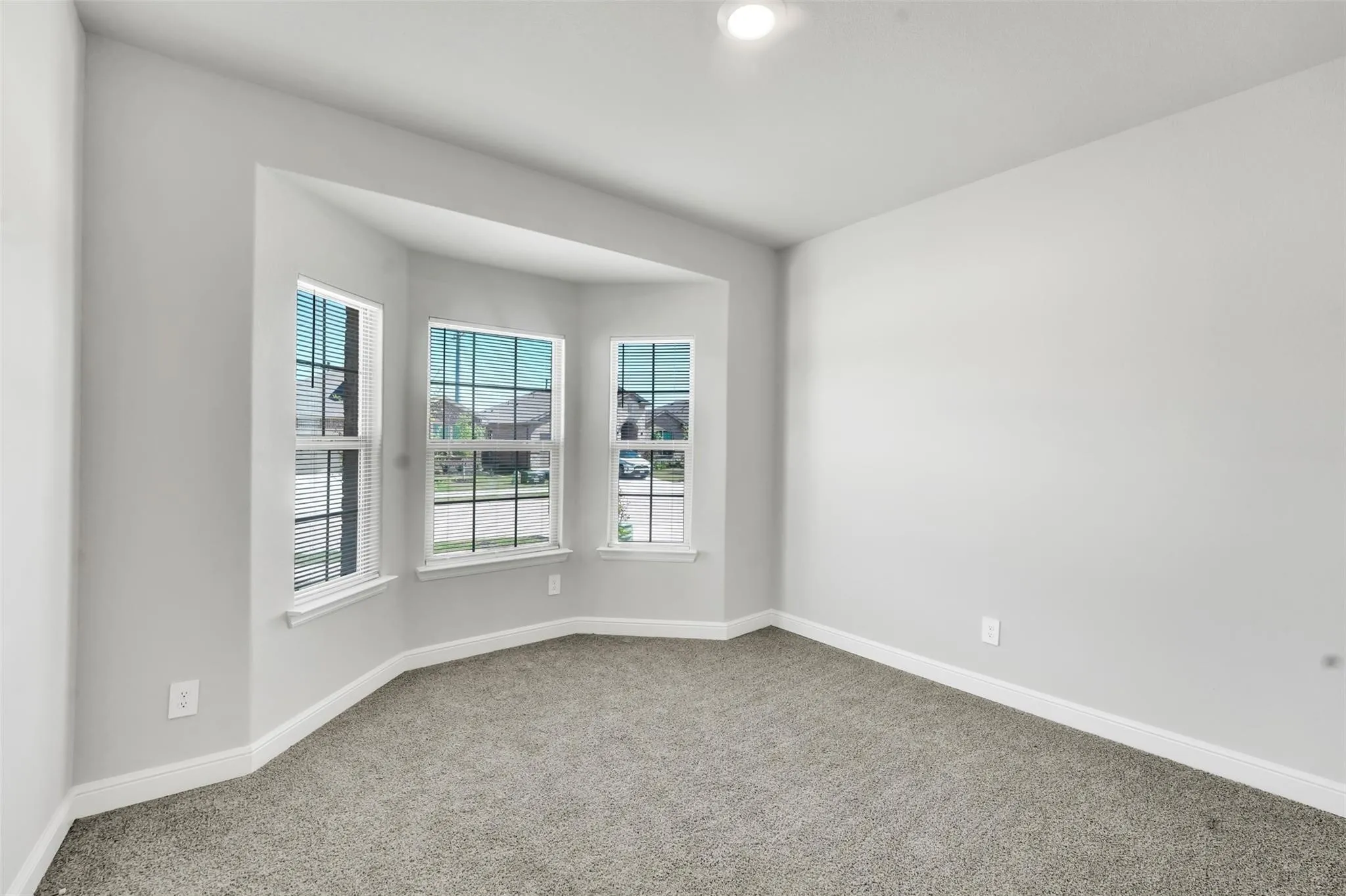 Spacious room featuring a three-panel bay window with white trim, light gray painted walls, recessed lighting, and gray carpet flooring