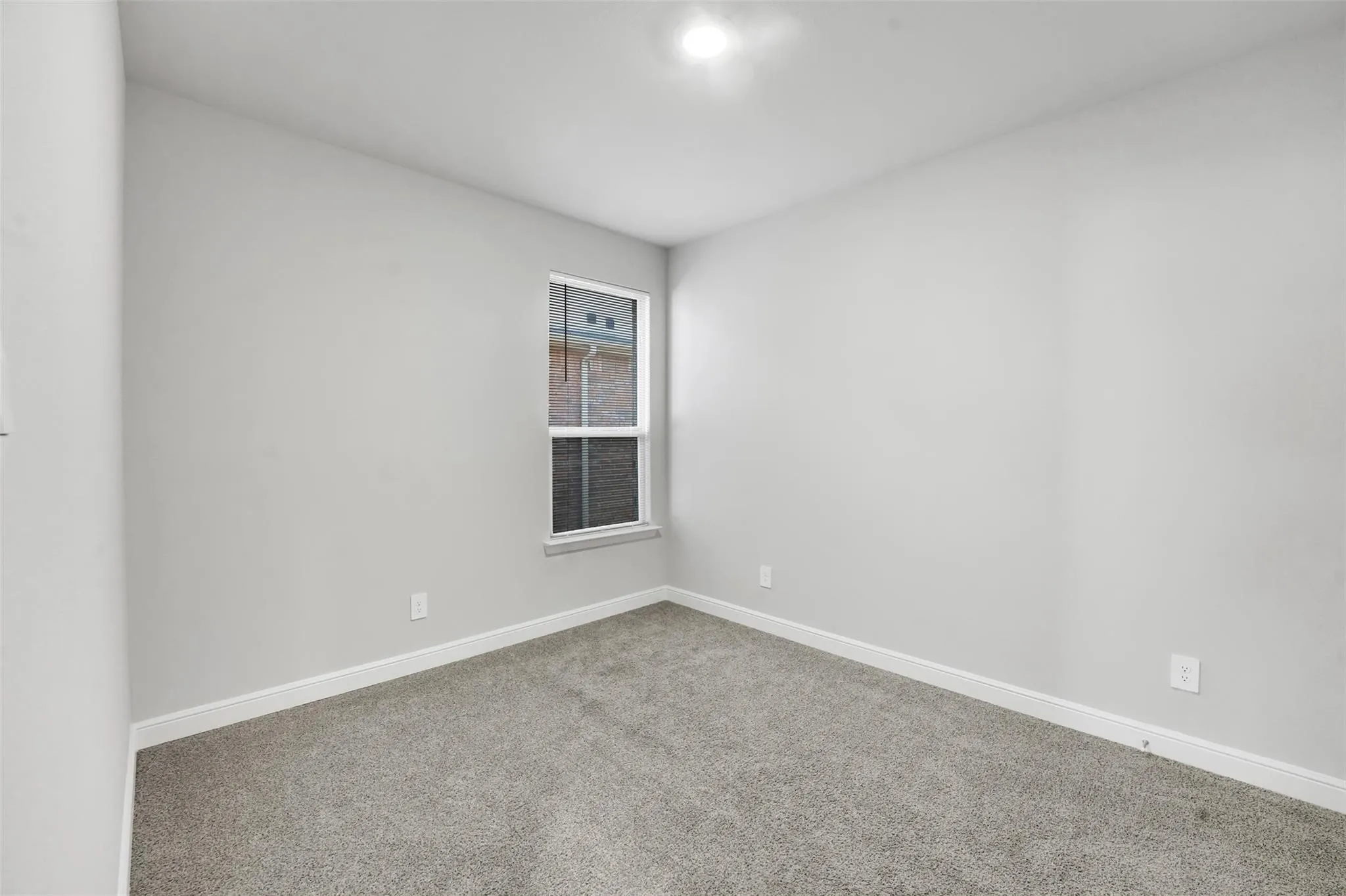 Neutral gray walls with white trim, gray carpet flooring, and a single window with white framing