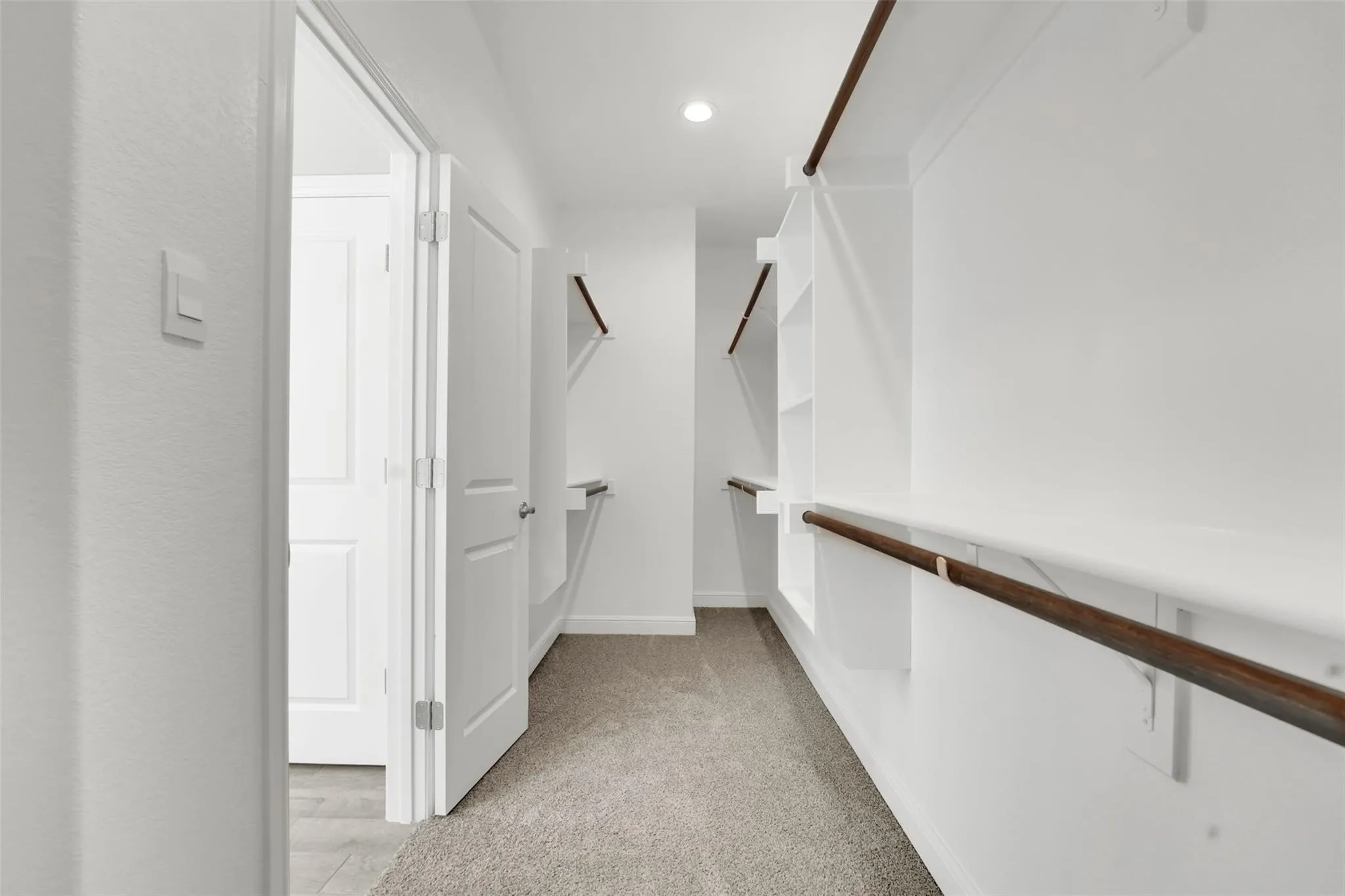 Walk-in closet featuring light gray carpet flooring, white walls, recessed lighting, and built-in white shelving with wood-finish hanging rods