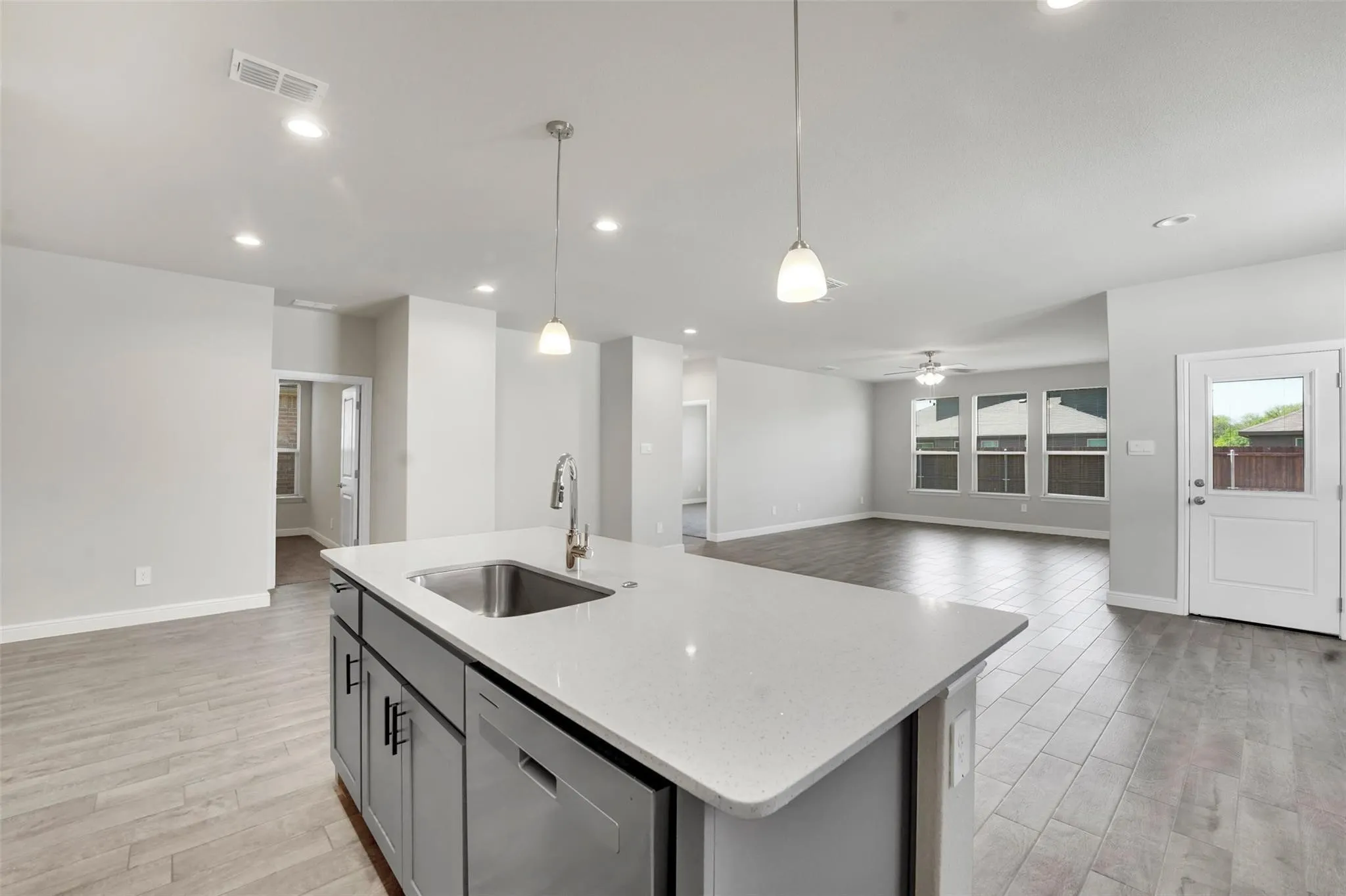 Kitchen island featuring a stainless steel sink with a gooseneck faucet, light-toned countertop, and gray cabinetry