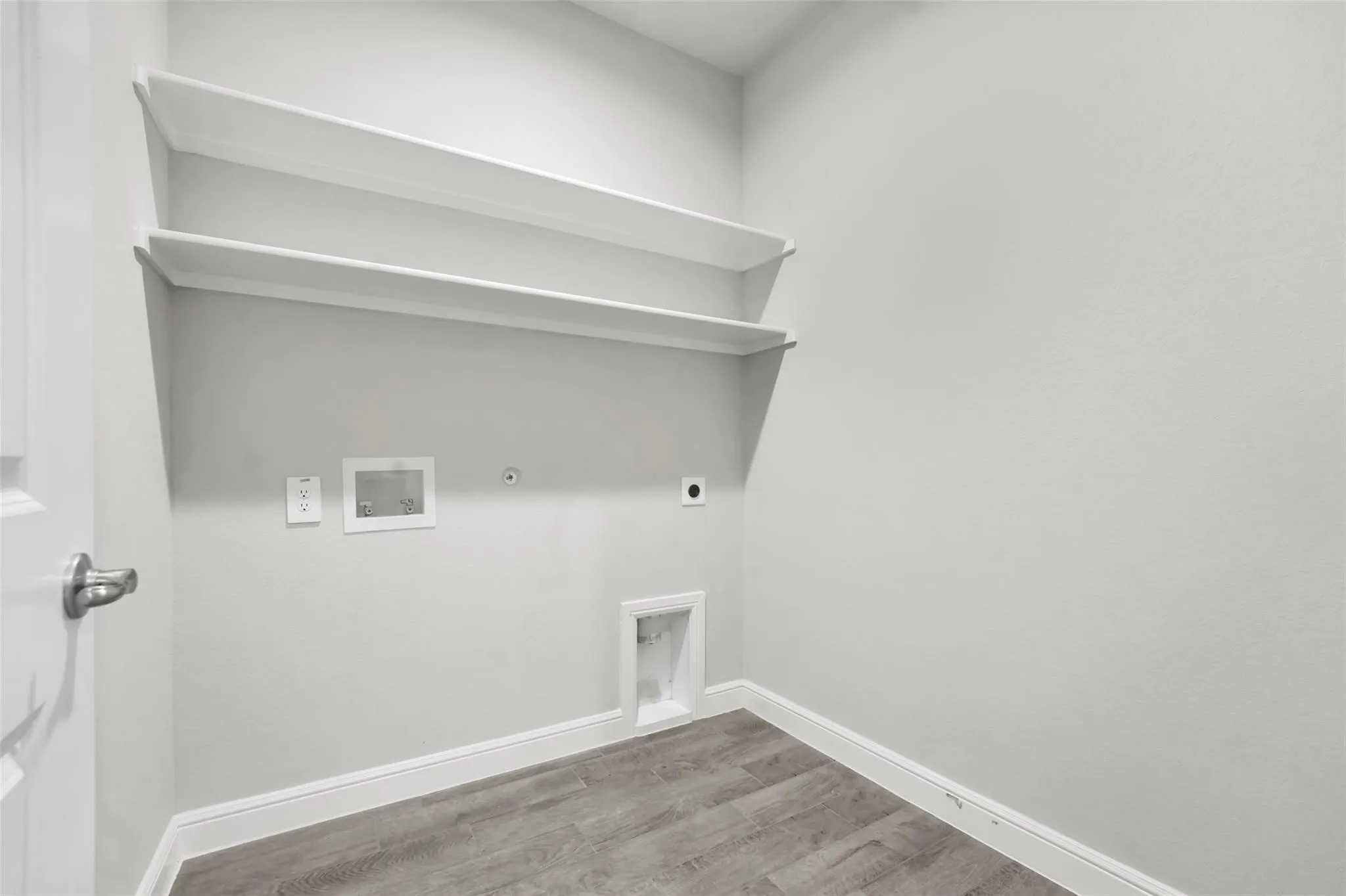 Dedicated laundry area featuring white shelving, light gray walls, wood-finish flooring, and white baseboards
