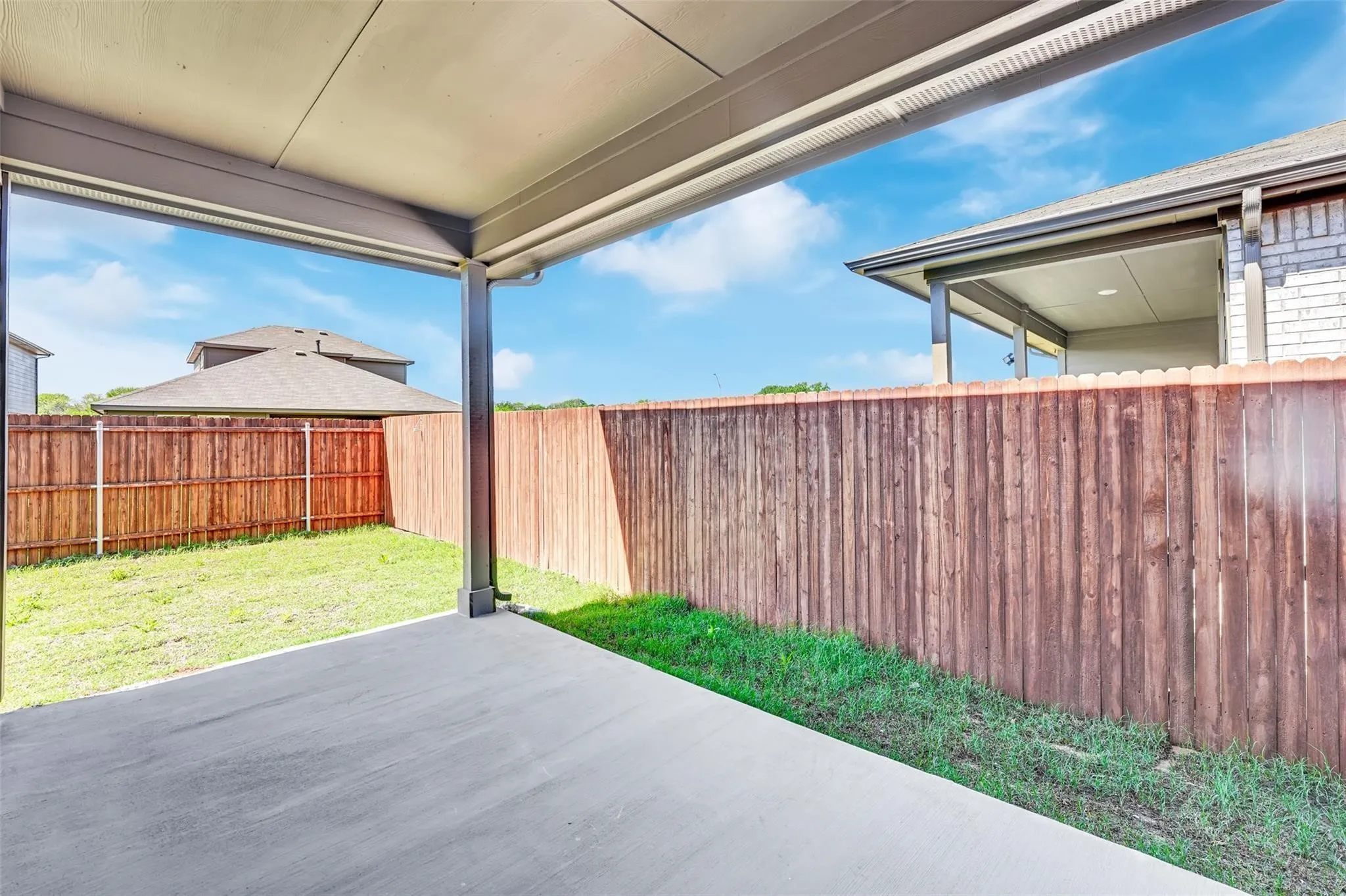 Covered concrete patio opening to a fenced backyard with a grass lawn