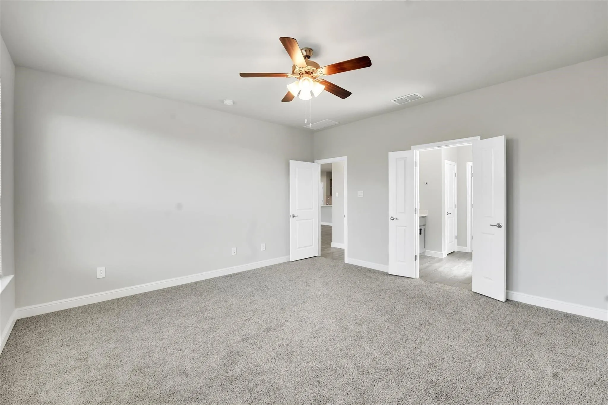 Spacious room featuring vaulted ceilings, a ceiling fan with light fixture, gray carpet flooring, white baseboards, and multiple white panel doors