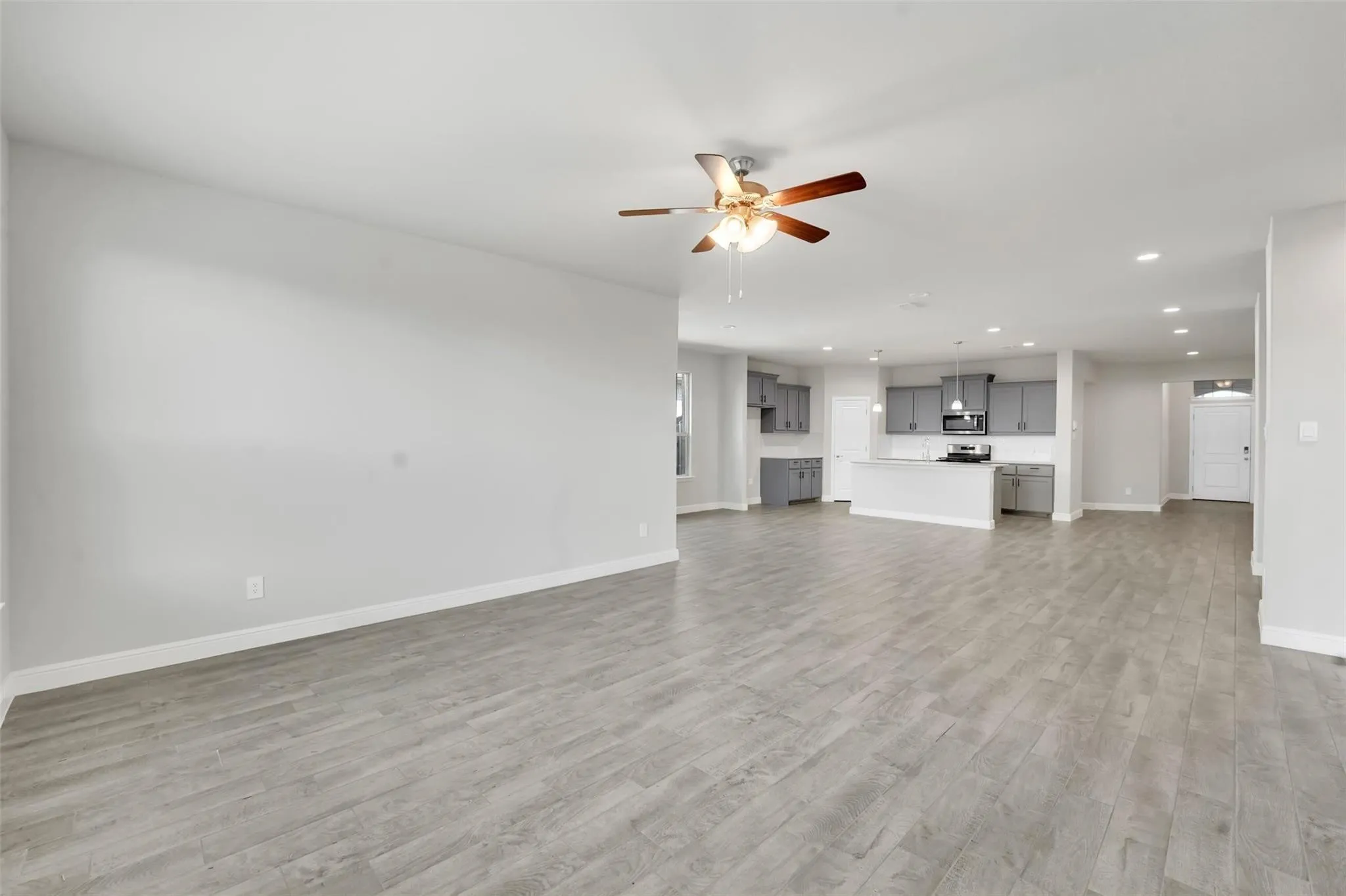 Expansive open-concept room featuring wood-finish flooring and a ceiling fan with integrated lighting