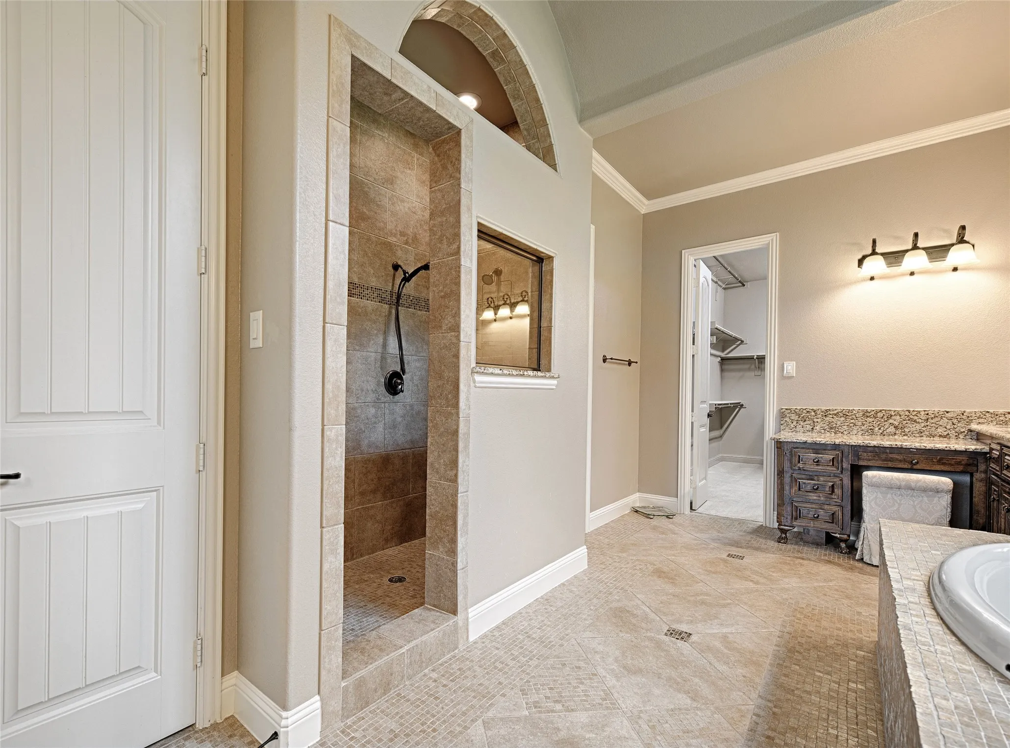Expansive tile shower with dark bronze fixtures and an arched stone-tiled accent