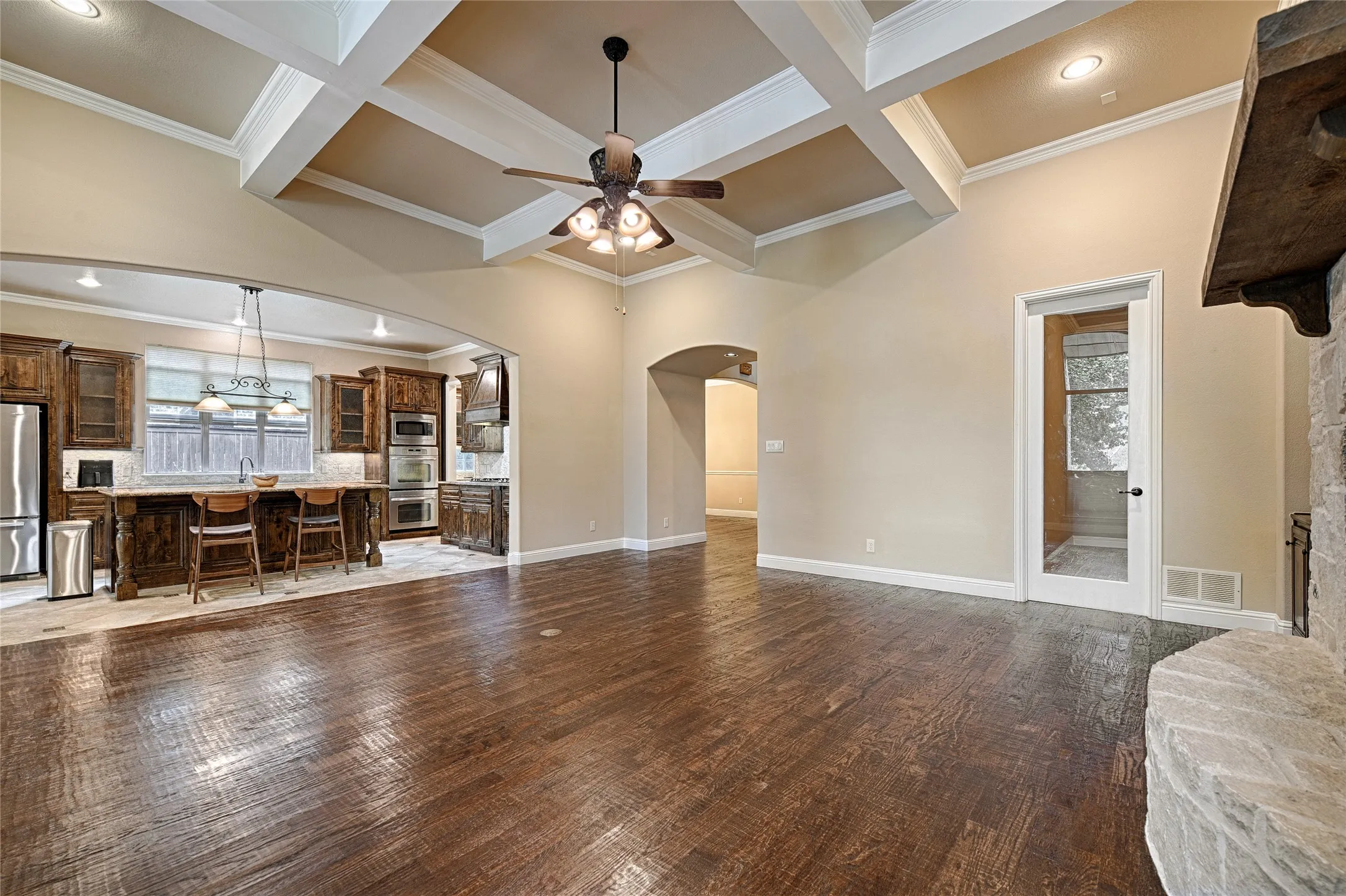 Spacious living area featuring wood-finish flooring, a coffered ceiling with a ceiling fan, and a stone fireplace with a substantial mantel