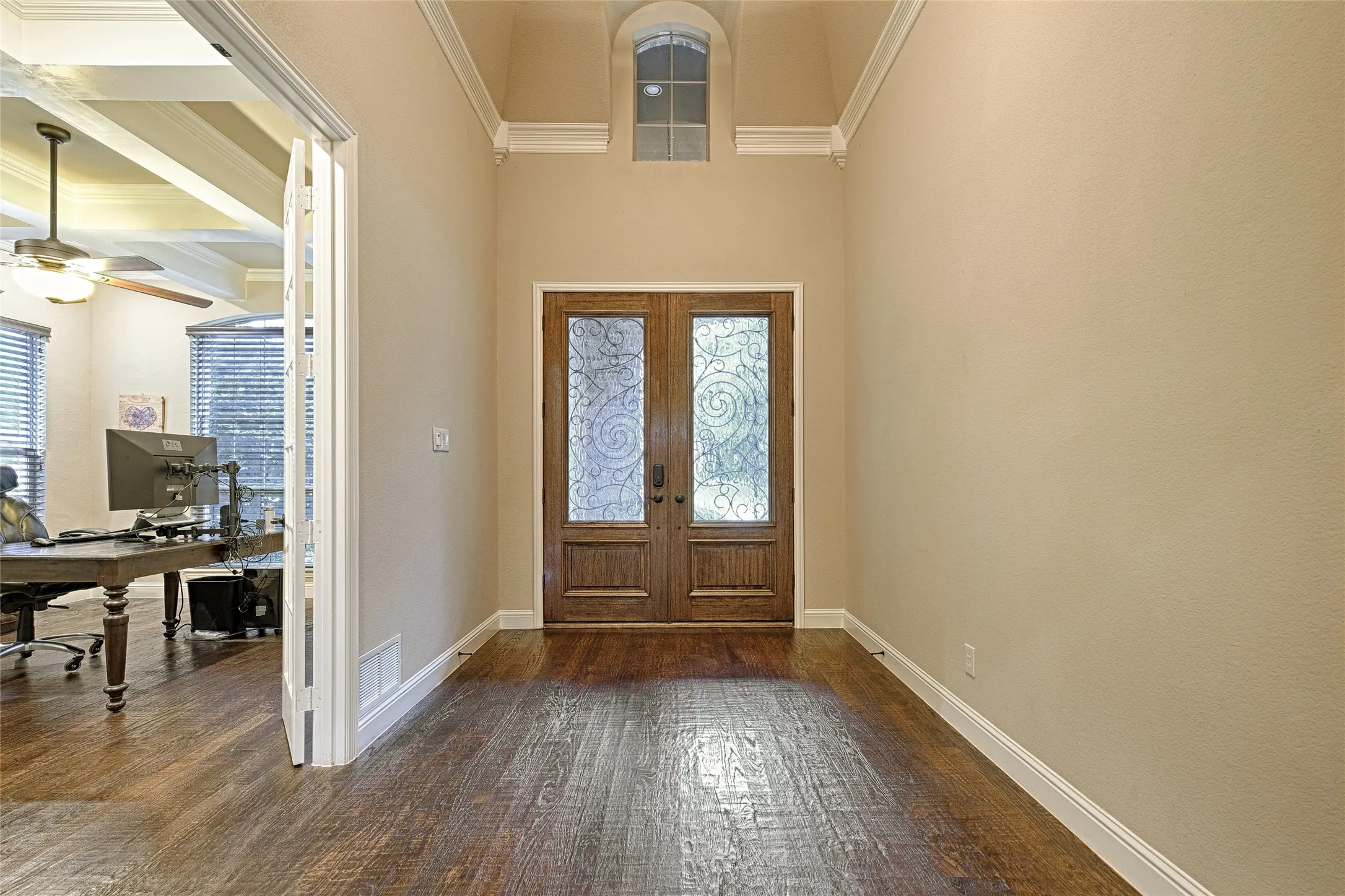 Grand entry hall featuring double wood-paneled doors with decorative glass inserts, a transom window, and high ceilings with crown molding