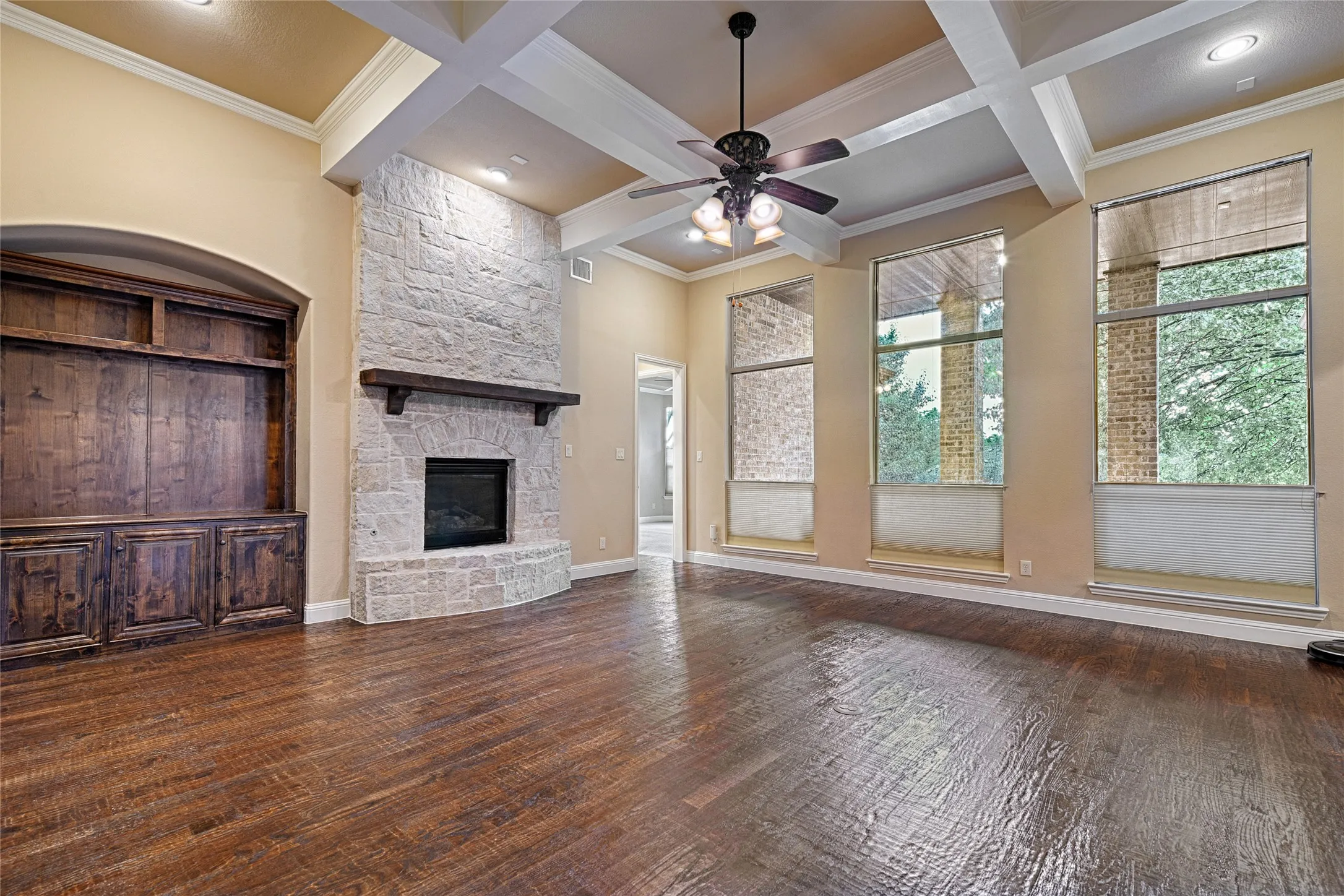 Living area featuring wood-finish flooring, a stone-clad fireplace with a dark wood mantel, built-in cabinetry, and a ceiling fan