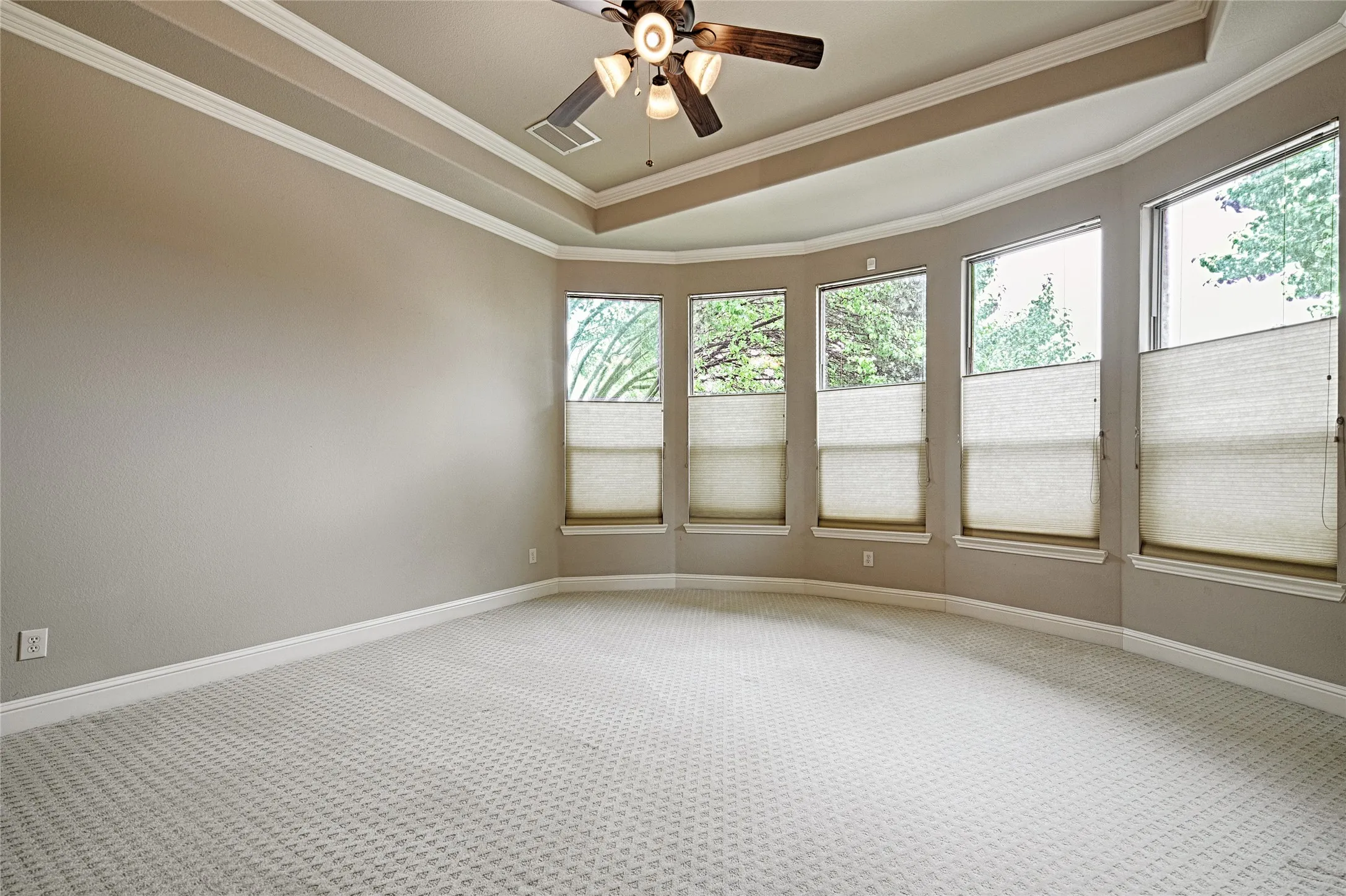 Spacious room featuring a tray ceiling with crown molding, a ceiling fan with integrated lighting, textured neutral walls, and light-patterned carpeting