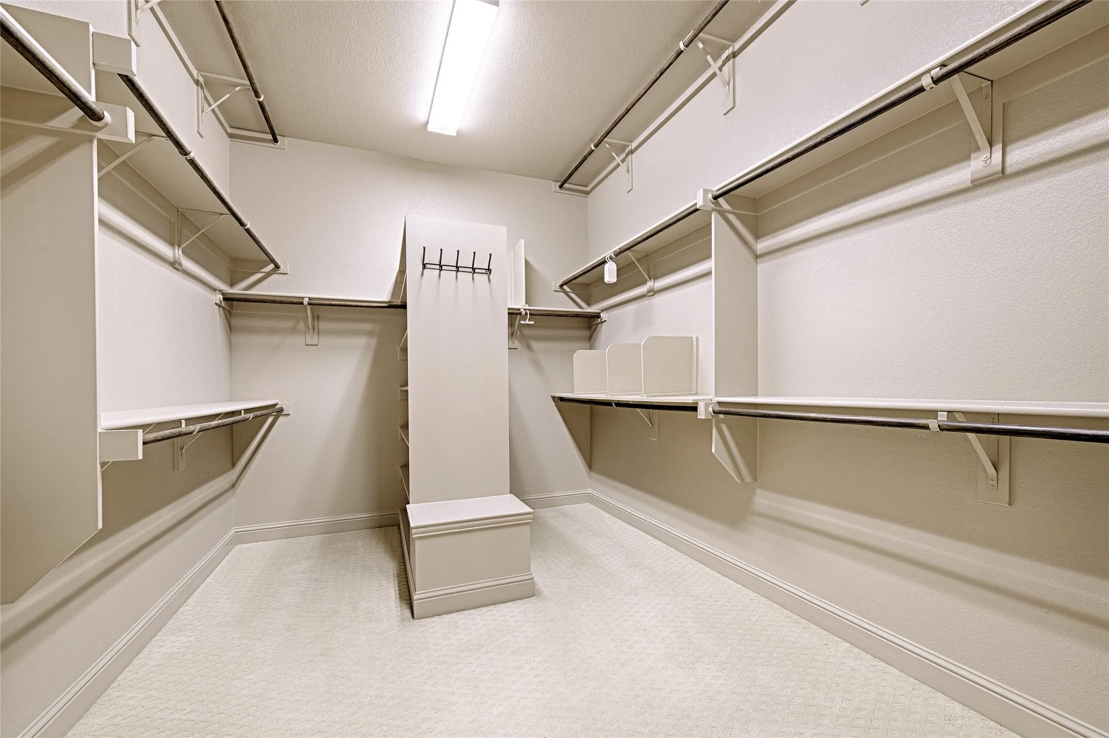 Spacious walk-in closet featuring extensive built-in shelving, multiple clothing rods, a central storage column with integrated shelving, a built-in bench, and plush carpeting