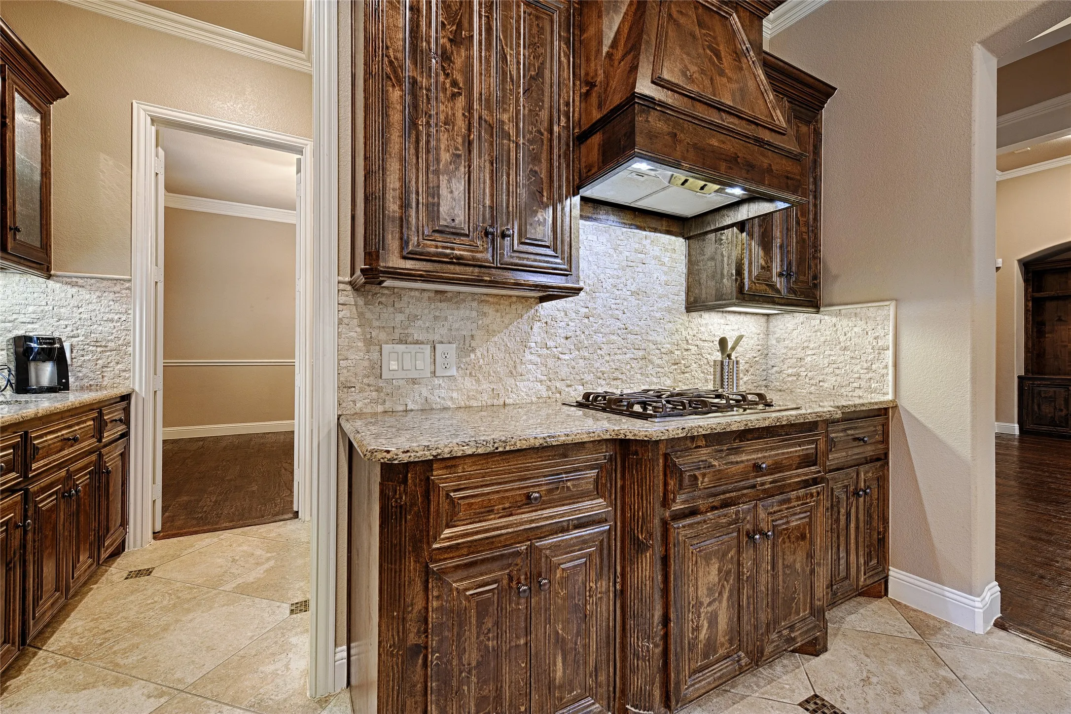 Kitchen featuring custom dark wood cabinetry, granite countertops, a tiled backsplash, and a built-in gas cooktop with an ornate wood vent hood