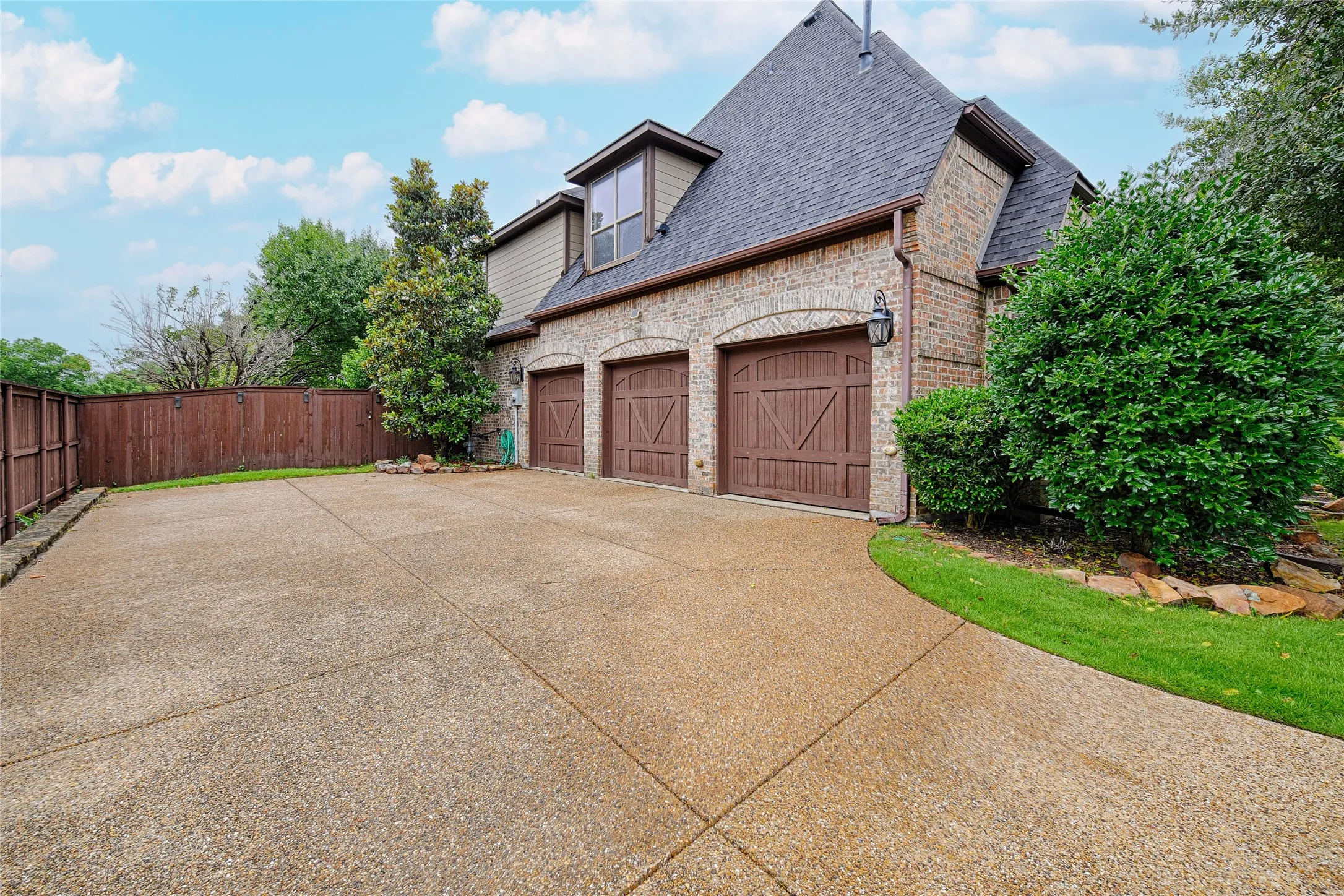 Brick and siding exterior featuring a three-car garage with arched entrances and wood-finish doors