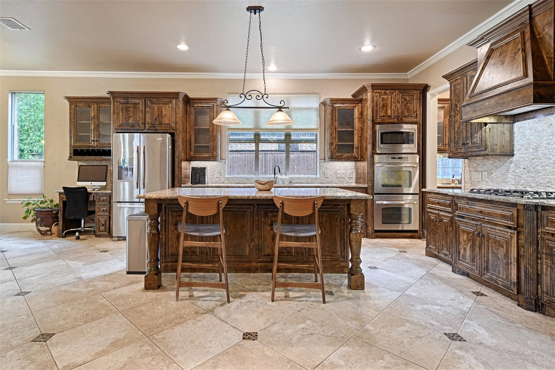 Gourmet kitchen featuring a large central island with seating, extensive wood cabinetry, integrated stainless steel appliances, and tile flooring with decorative inserts