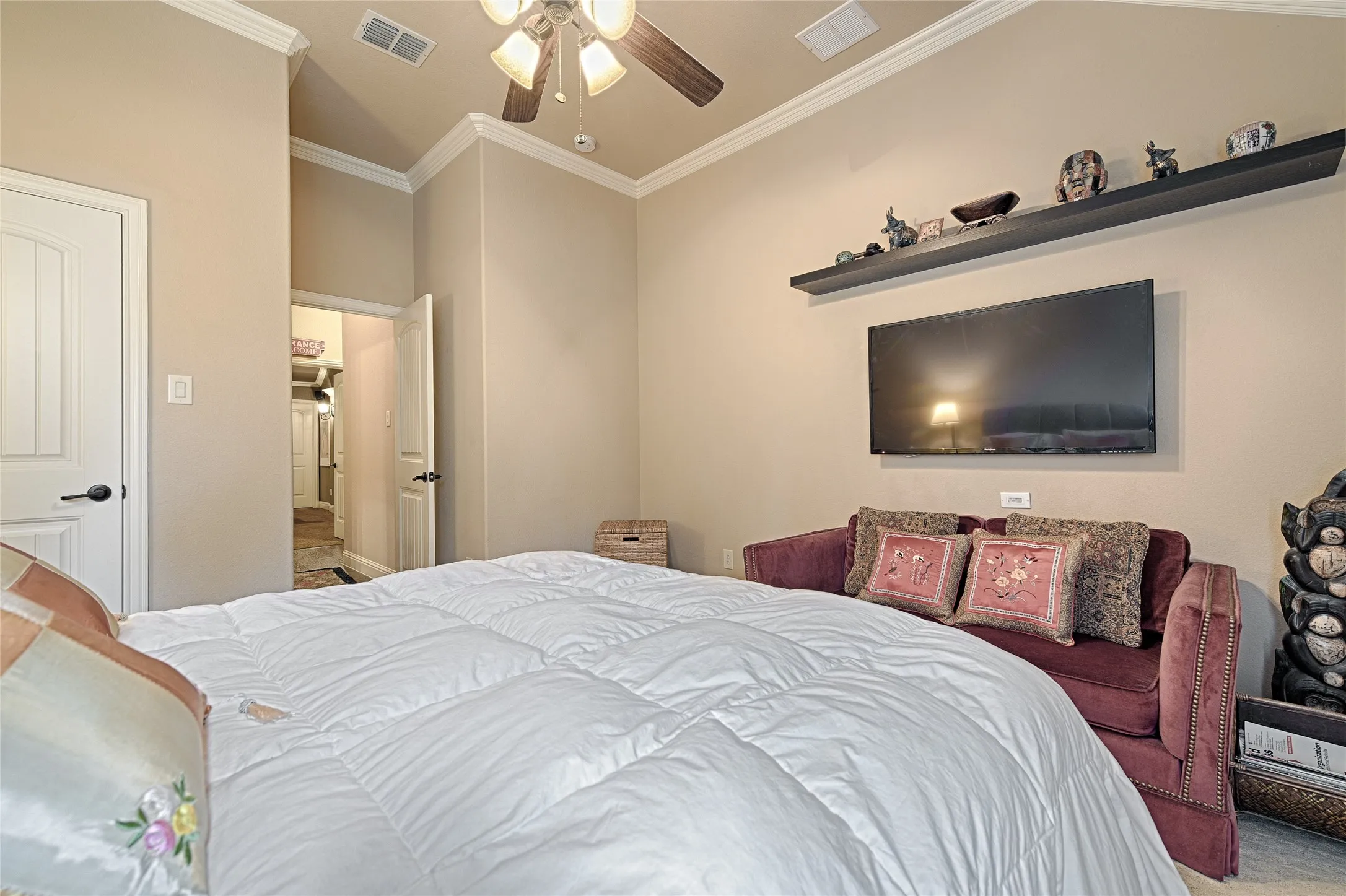 Bedroom featuring crown molding, a ceiling fan, a wall-mounted media display, and a recessed wall shelf