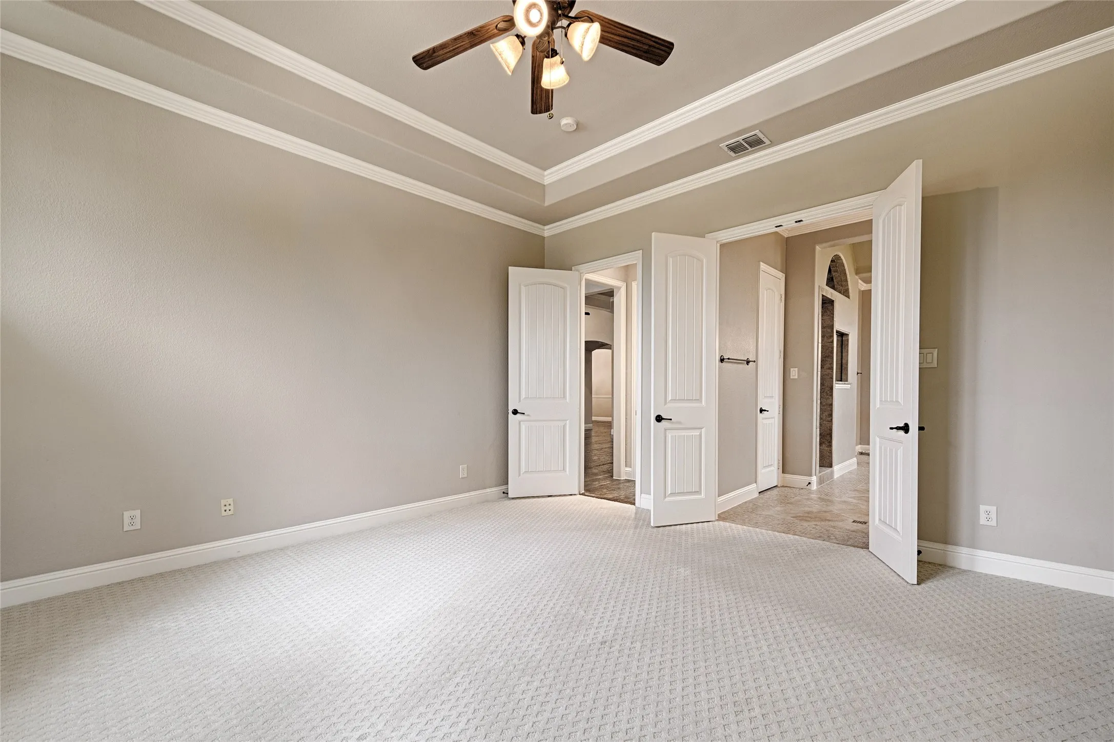 Spacious room featuring tray ceilings with crown molding, a ceiling fan with integrated lighting, textured wall finishes, and patterned carpet flooring