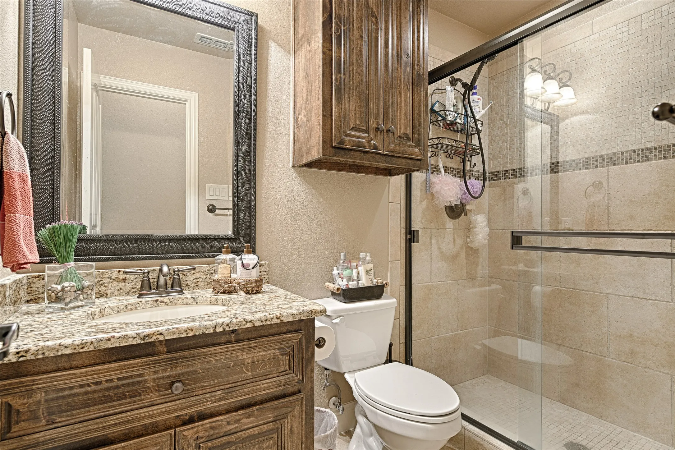 Bathroom featuring a walk-in shower with glass enclosure, a vanity with a granite countertop and an undermount sink, and wood-finish cabinetry