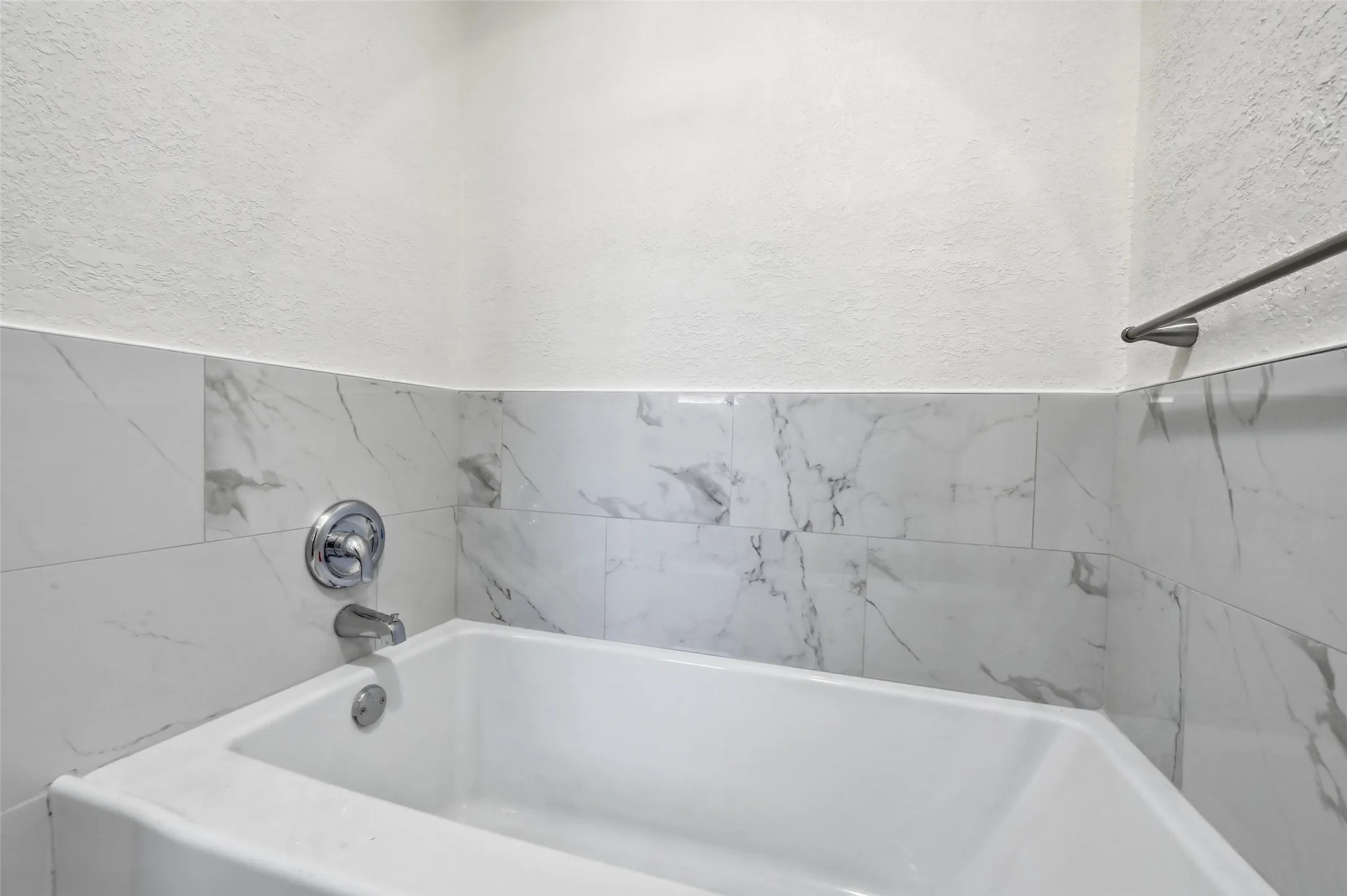 White bathtub with polished chrome fixtures, surrounded by white marble-look tile wainscoting