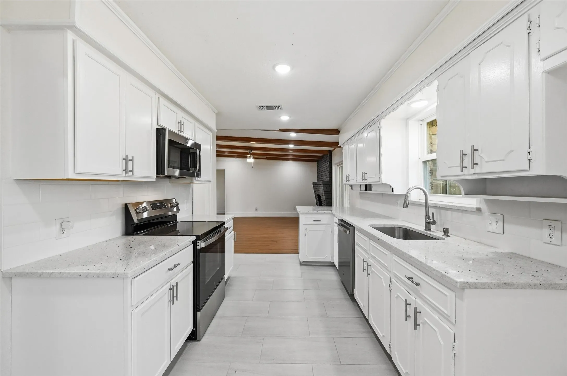 Galley kitchen featuring white cabinetry, light-toned countertops, stainless steel appliances, and tile flooring