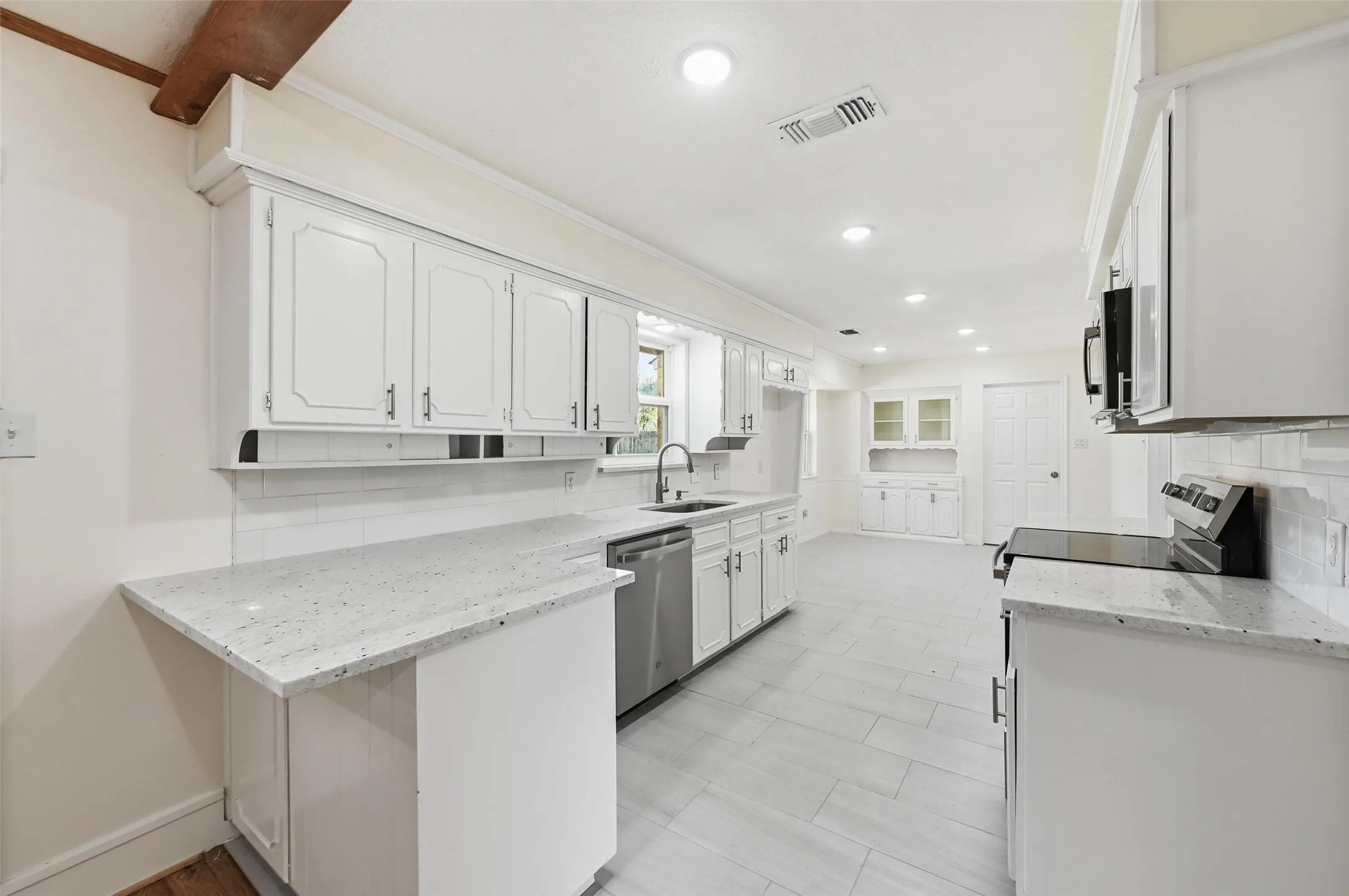 Bright kitchen featuring white cabinetry, light-toned countertops, subway tile backsplash, and stainless steel appliances