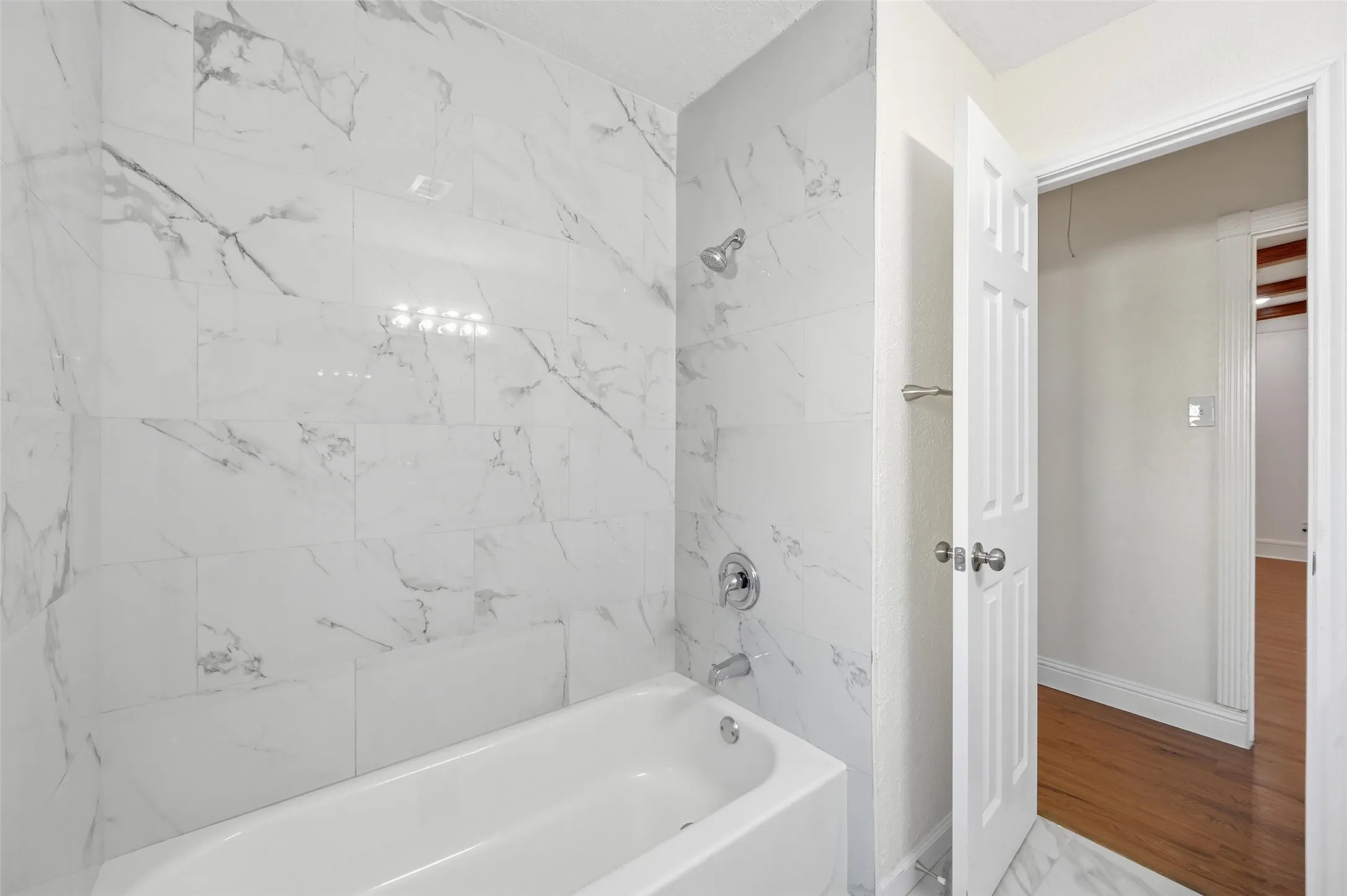 Bathtub with polished chrome fixtures and white marble-look subway tile surround