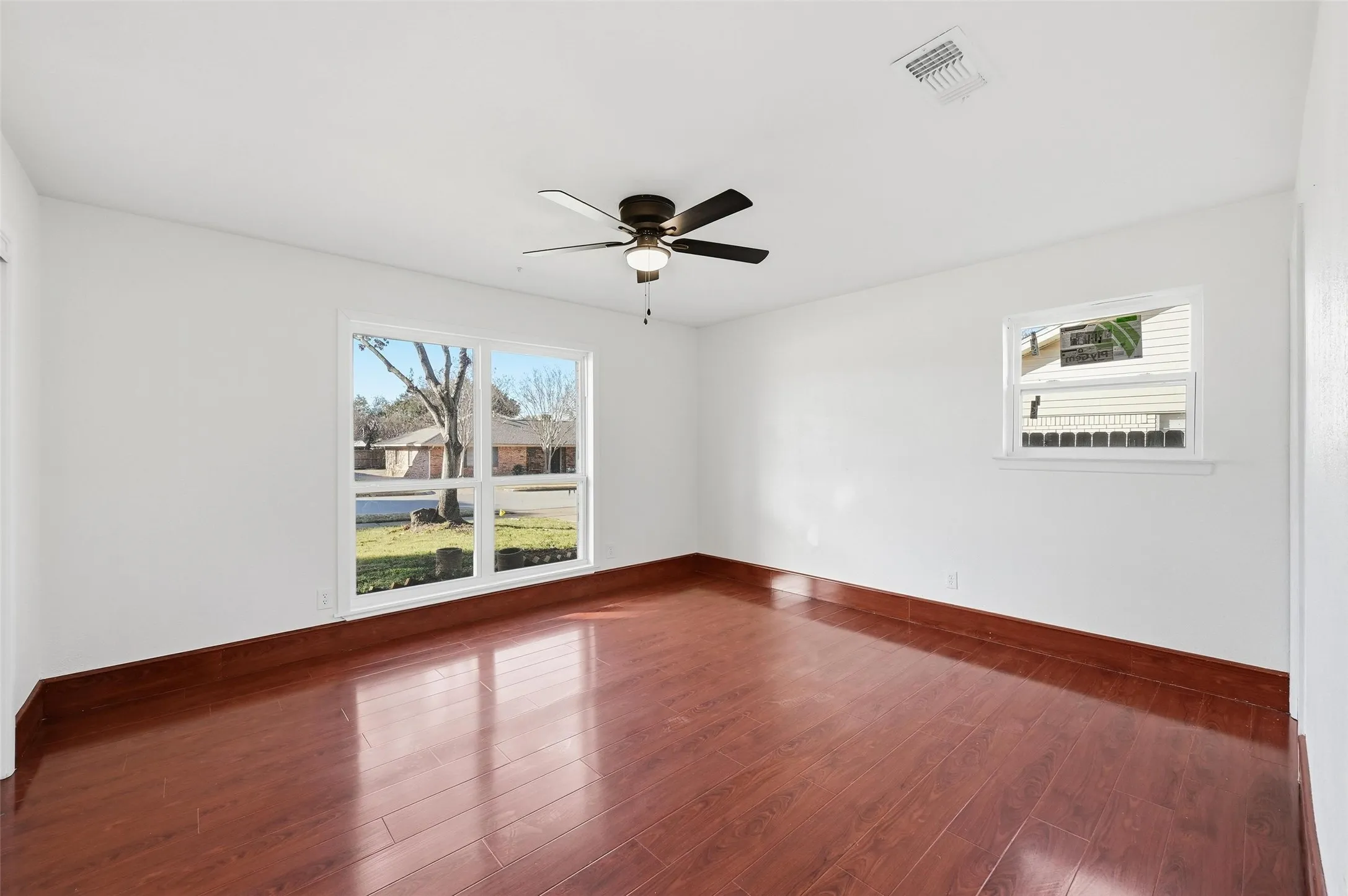 Bright room featuring wood-finish flooring, white walls, and a ceiling fan with integrated lighting