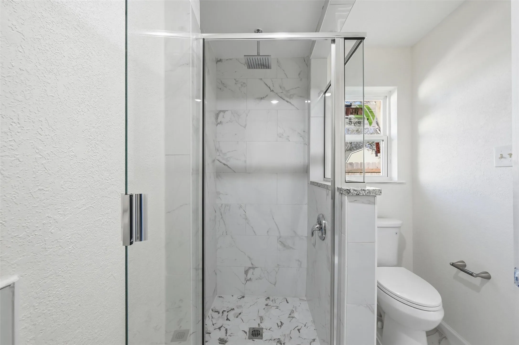 Glass-enclosed shower with white marble-style tile walls and a rainfall showerhead