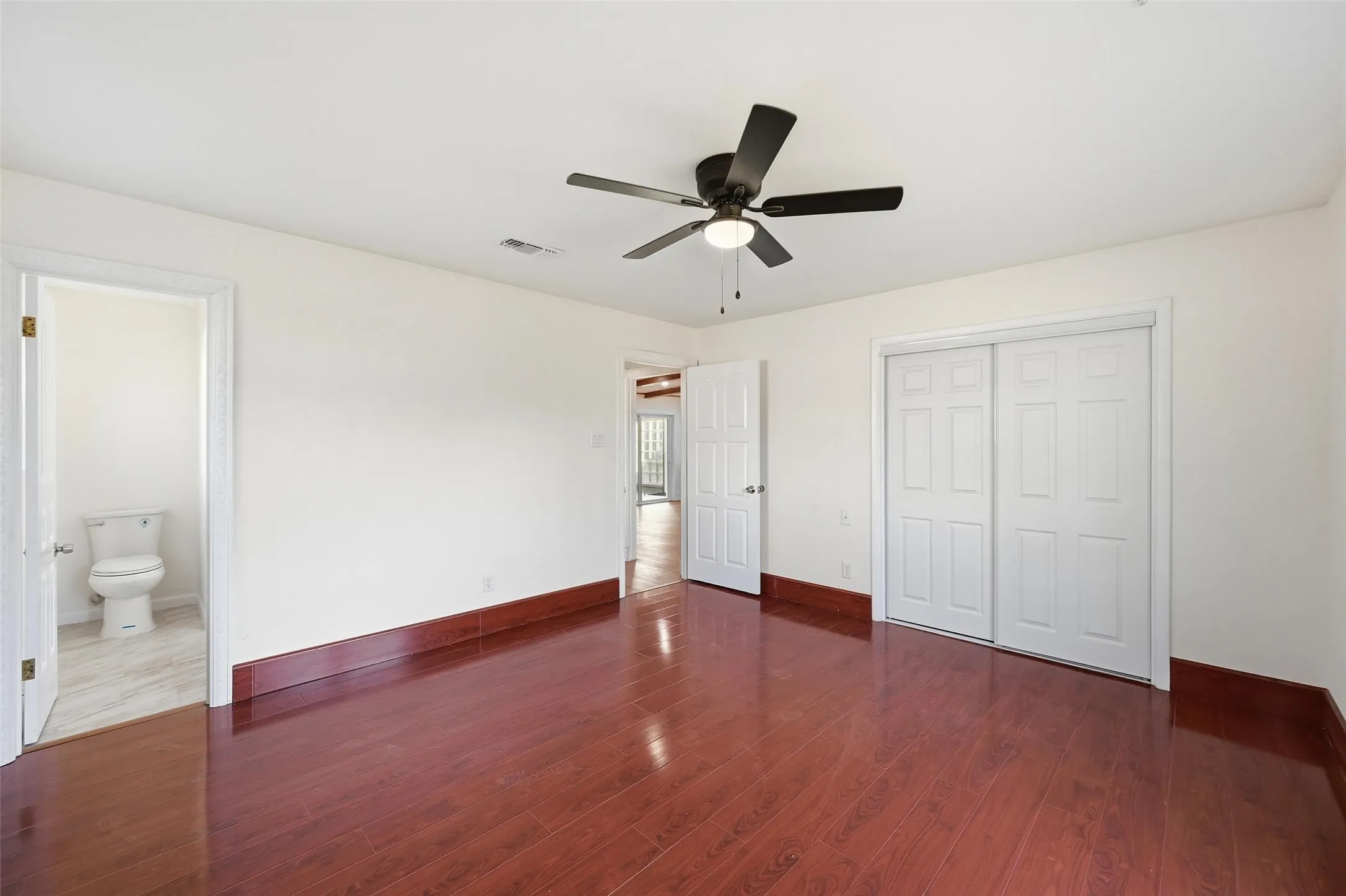 Spacious room featuring wood-finish flooring, white walls, and a dark ceiling fan with integrated lighting