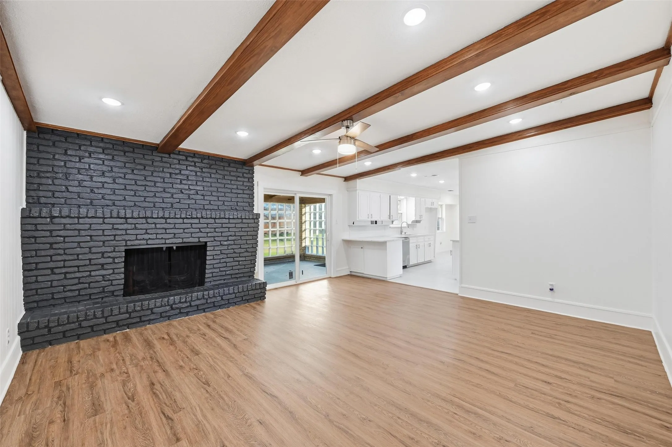 Spacious living area featuring a dark brick fireplace, wood-finish flooring, and exposed wood beams