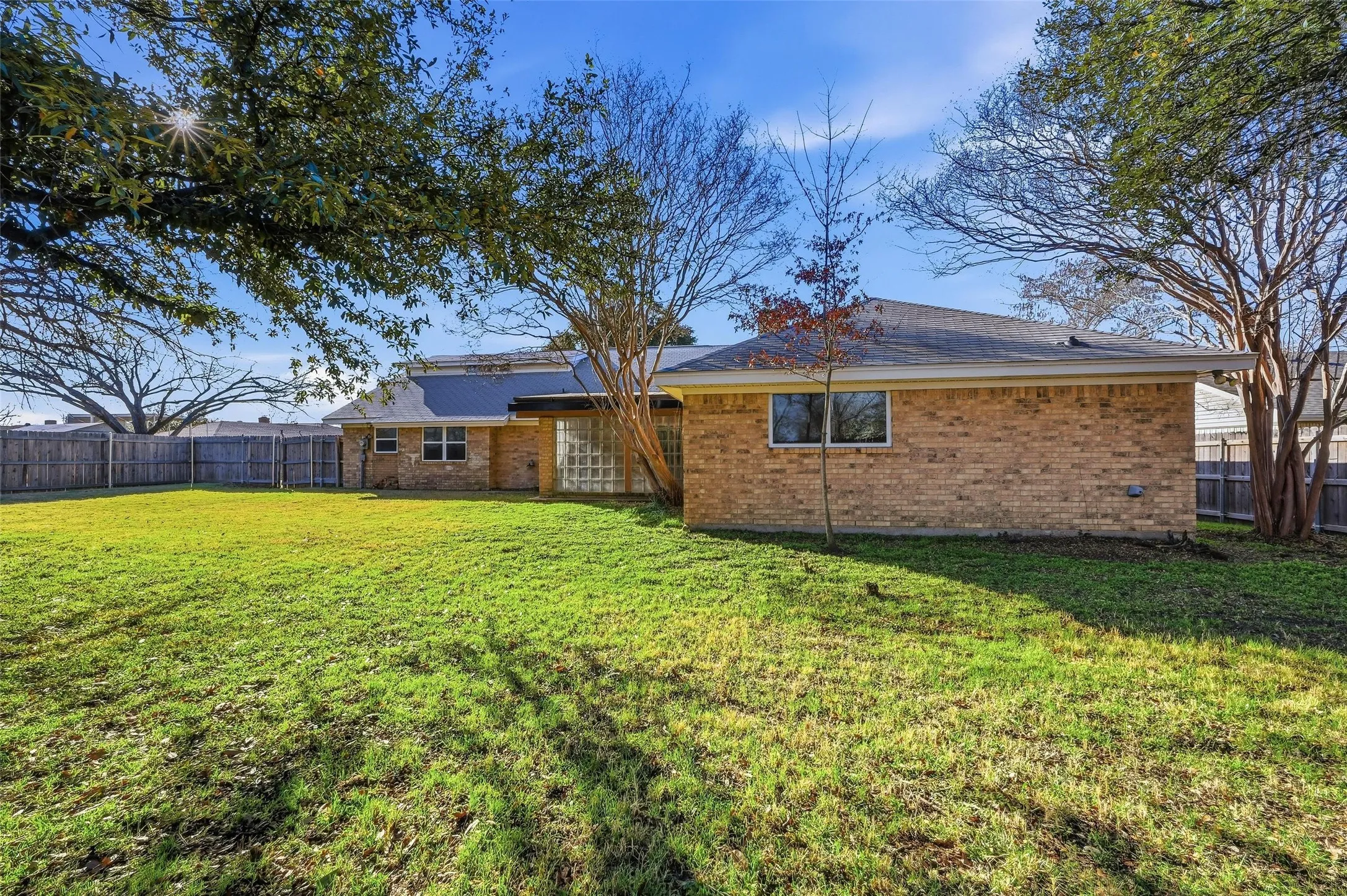 Expansive green lawn with mature trees and a privacy fence enclosing the property