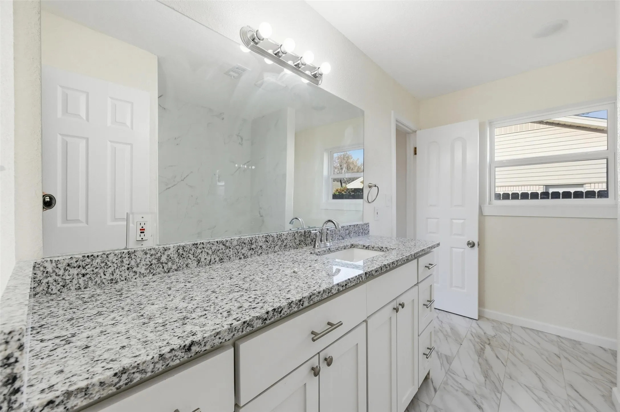 Double vanity with light granite countertops, polished chrome fixtures, and white cabinetry