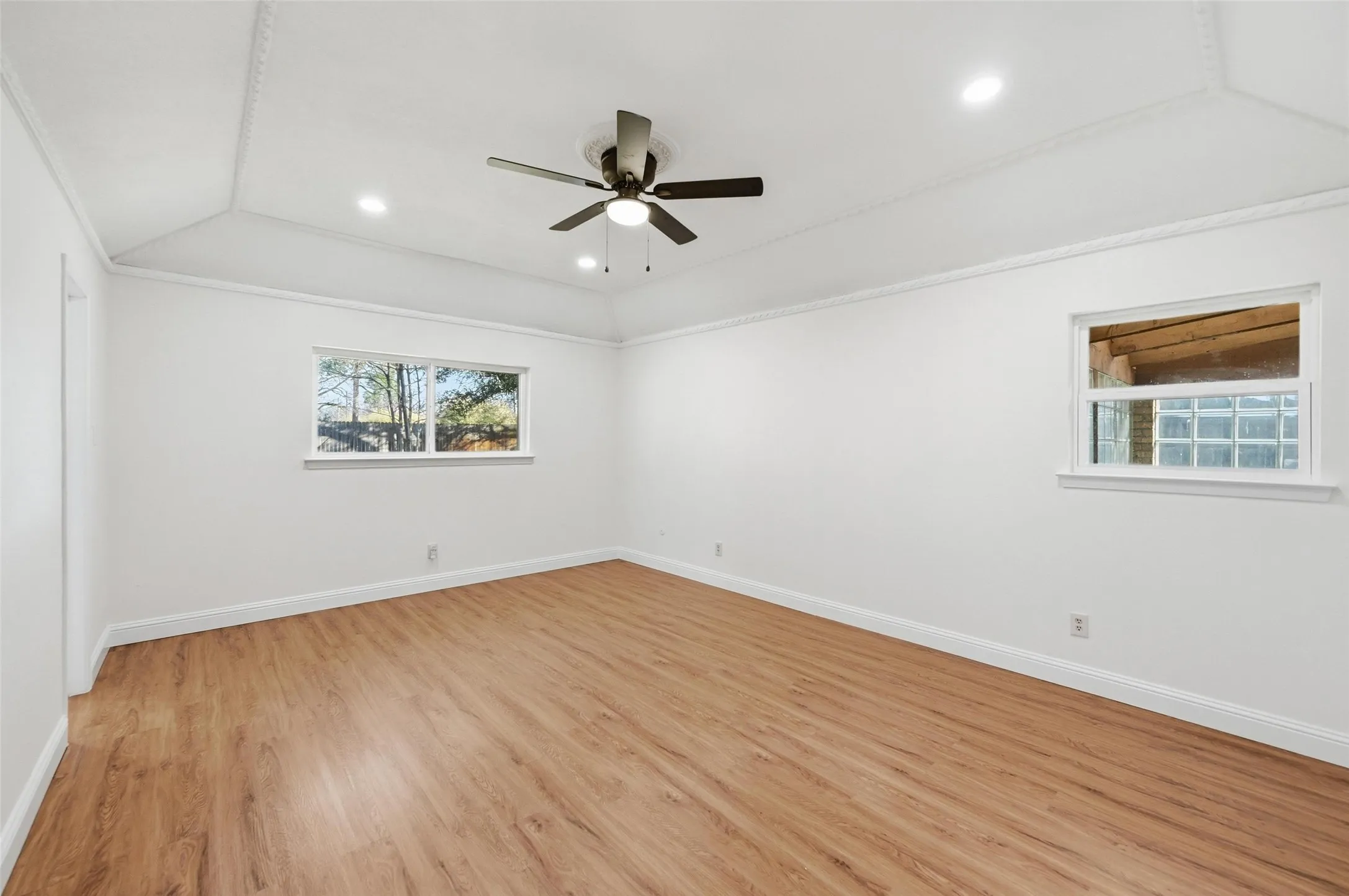 Spacious room featuring wood-finish flooring, a vaulted ceiling with crown molding, and recessed lighting