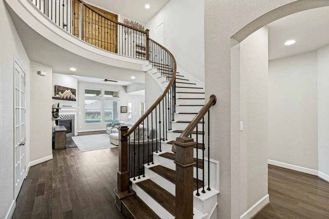 Grand foyer featuring a curved staircase with wrought iron balusters and wood-finish handrail, dark wood-finish flooring, recessed lighting, and an arched entry